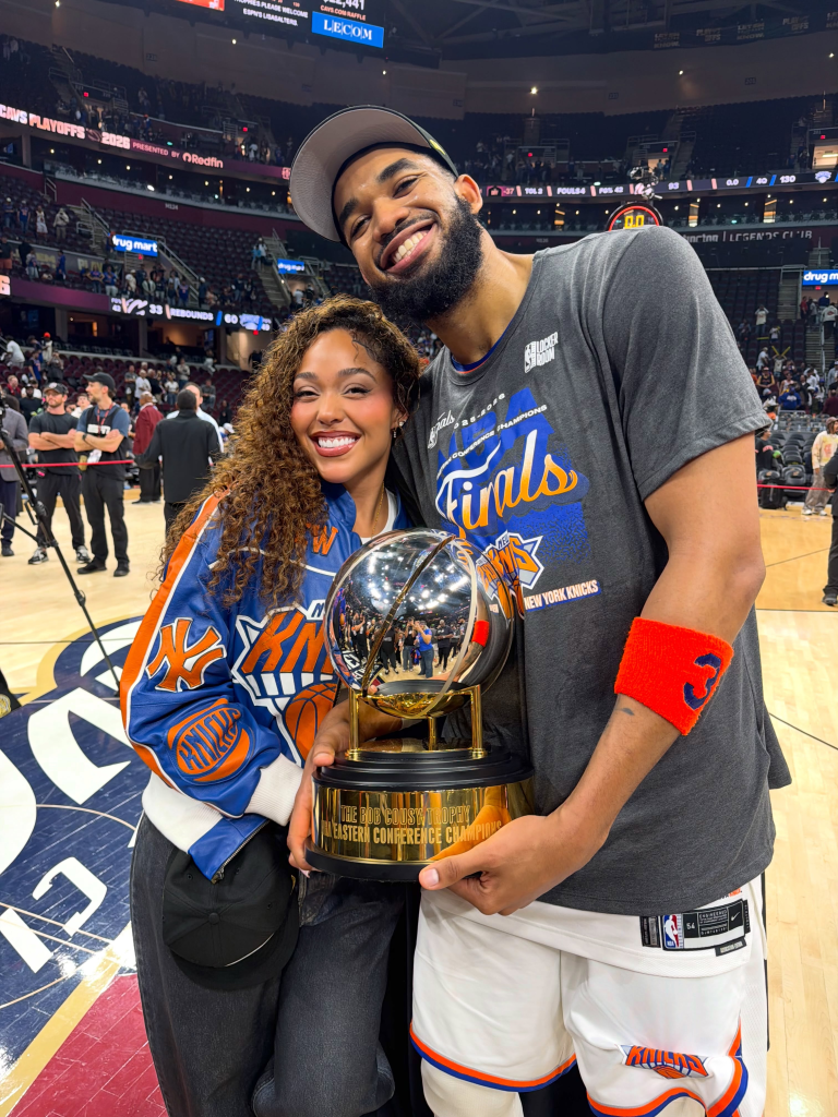 Jordyn Woods and Karl-Anthony Towns hold the Eastern Conference Championship trophy on a basketball court.