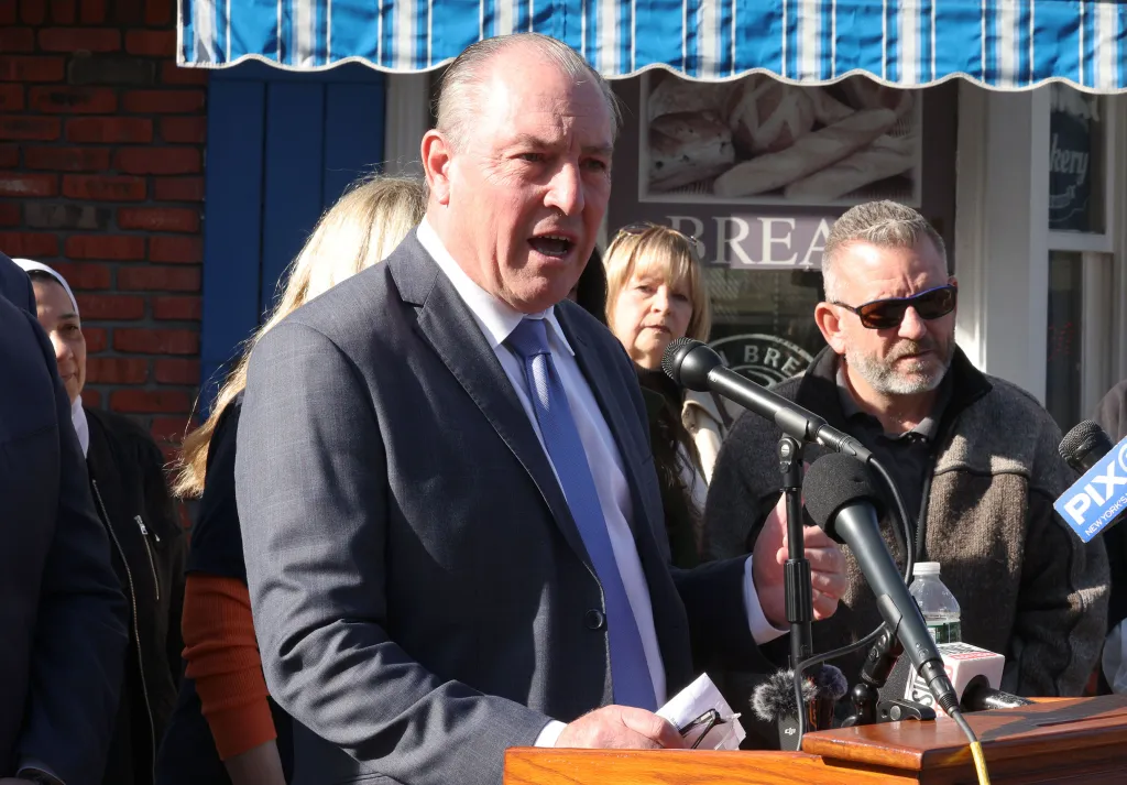 Staten Island Borough President Vito Fossella speaks at a bakery, with onlookers and microphones in the foreground.