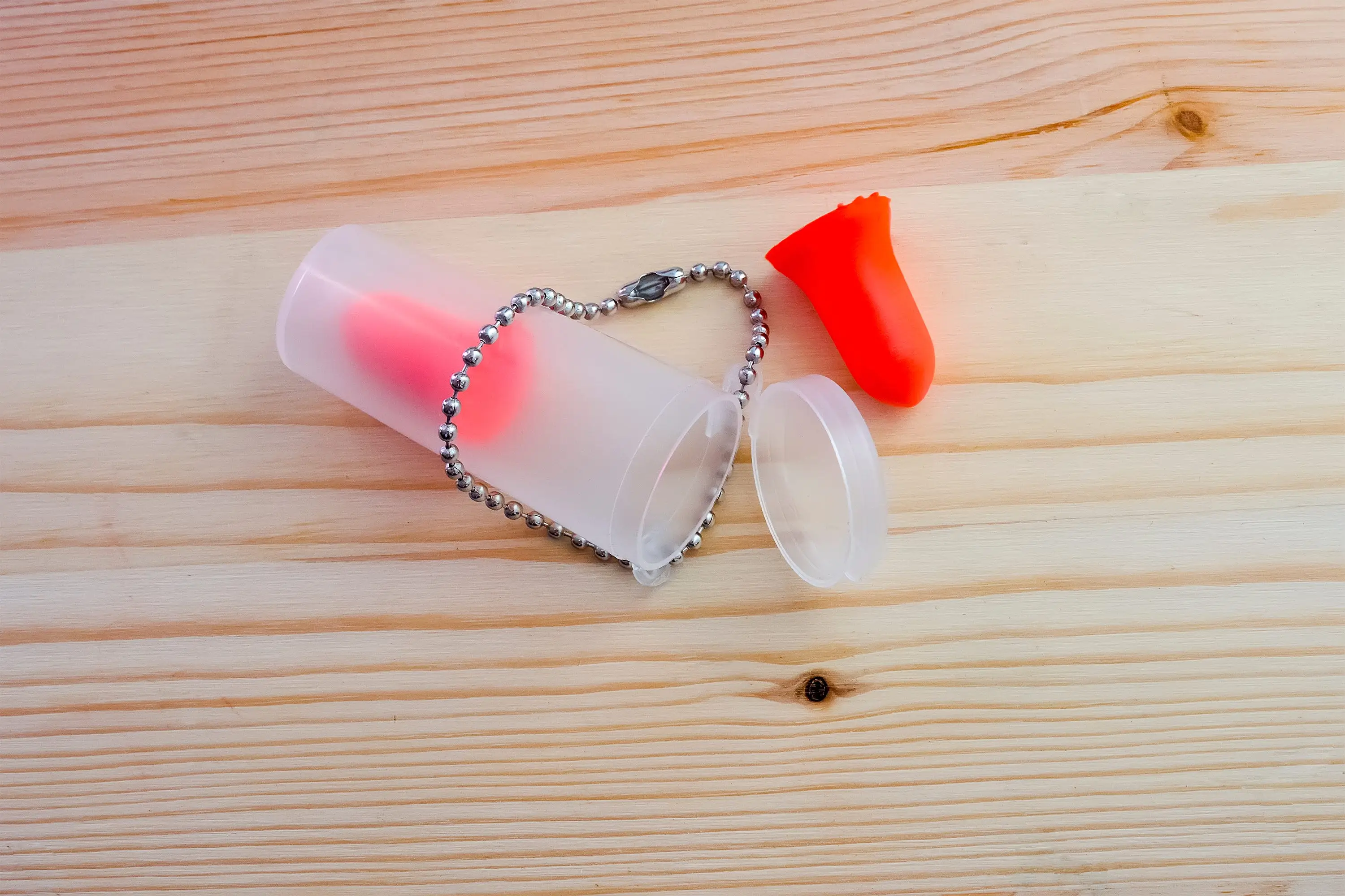 Red earplugs by plastic container on light wood table