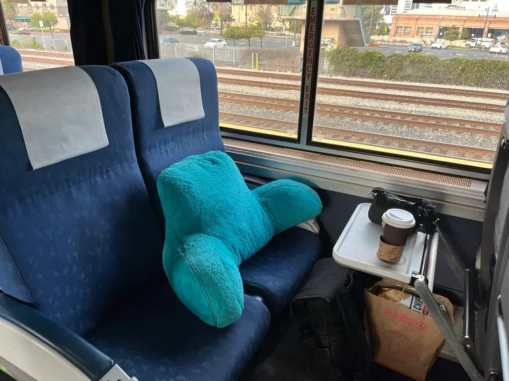 A turquoise bed-rest pillow sitting on an Amtrak train seat in front of a tray with a coffee cup on top.