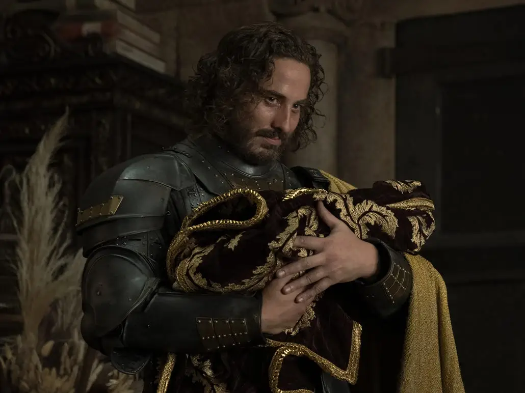 A man in armor holding a baby in a blanket.
