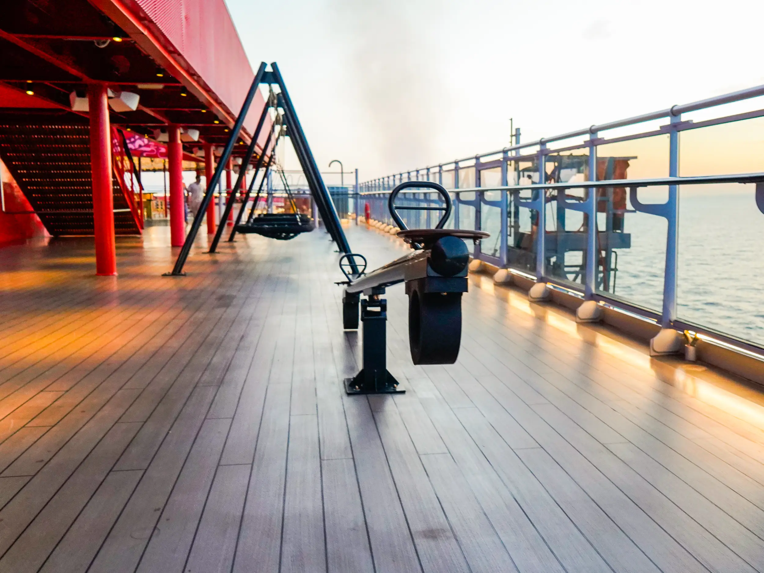 An empty deck on a cruise ship with a black seesaw, swings, and  a red staircase