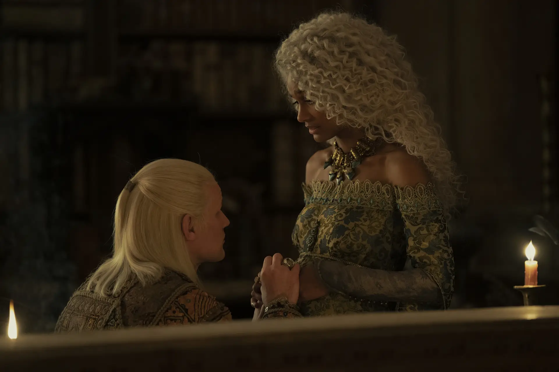 matt smith as daemon targaryen, kneeling in front of his pregnant wife, laena targaryen, played by nanna blondell. daemon has his hands over laena's belly, and she's looking down at him