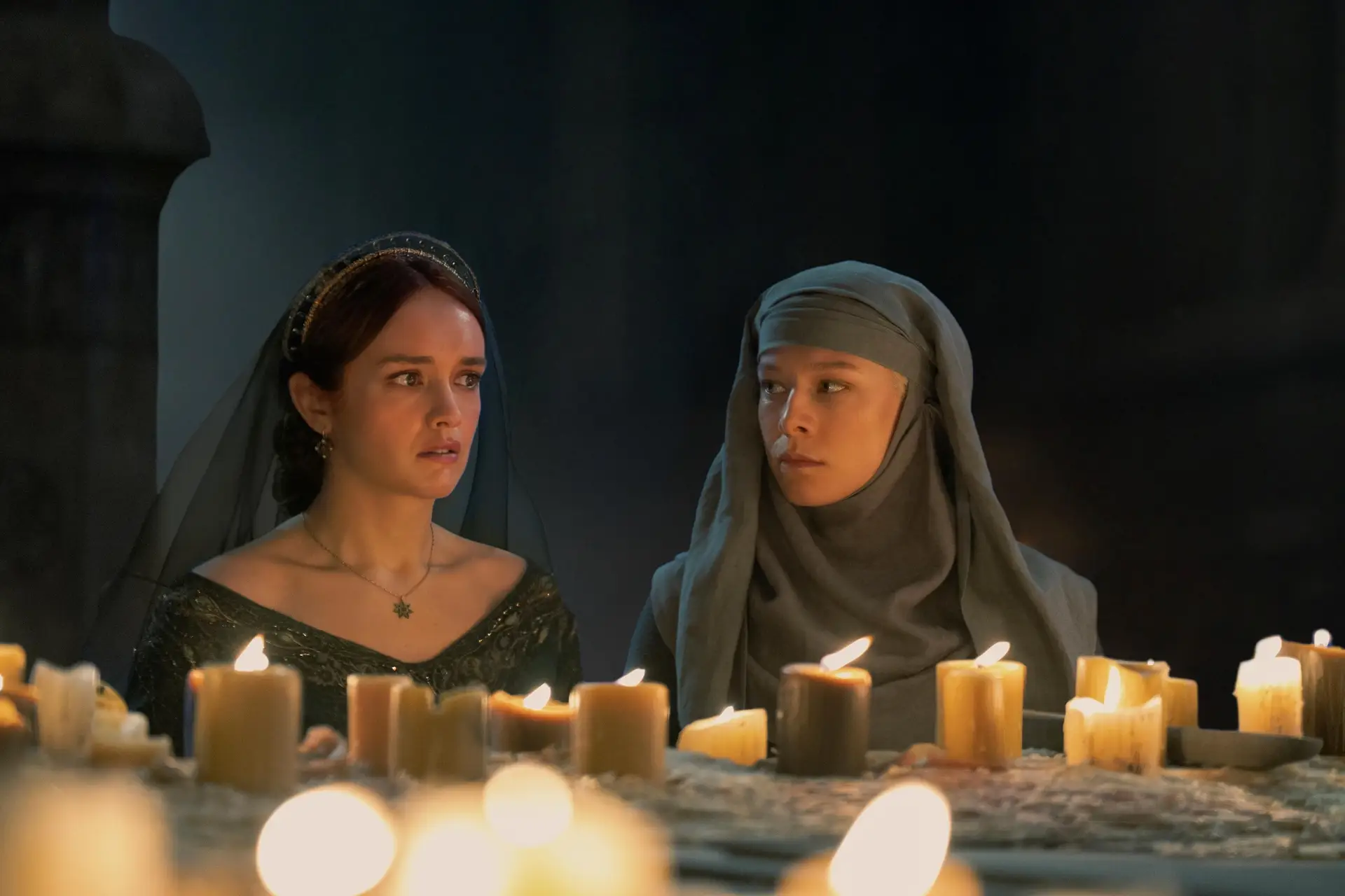 Olivia Cooke as Alicent and Emma D'Arcy as Rhaenyra in front of multiple candles in a dark room.
