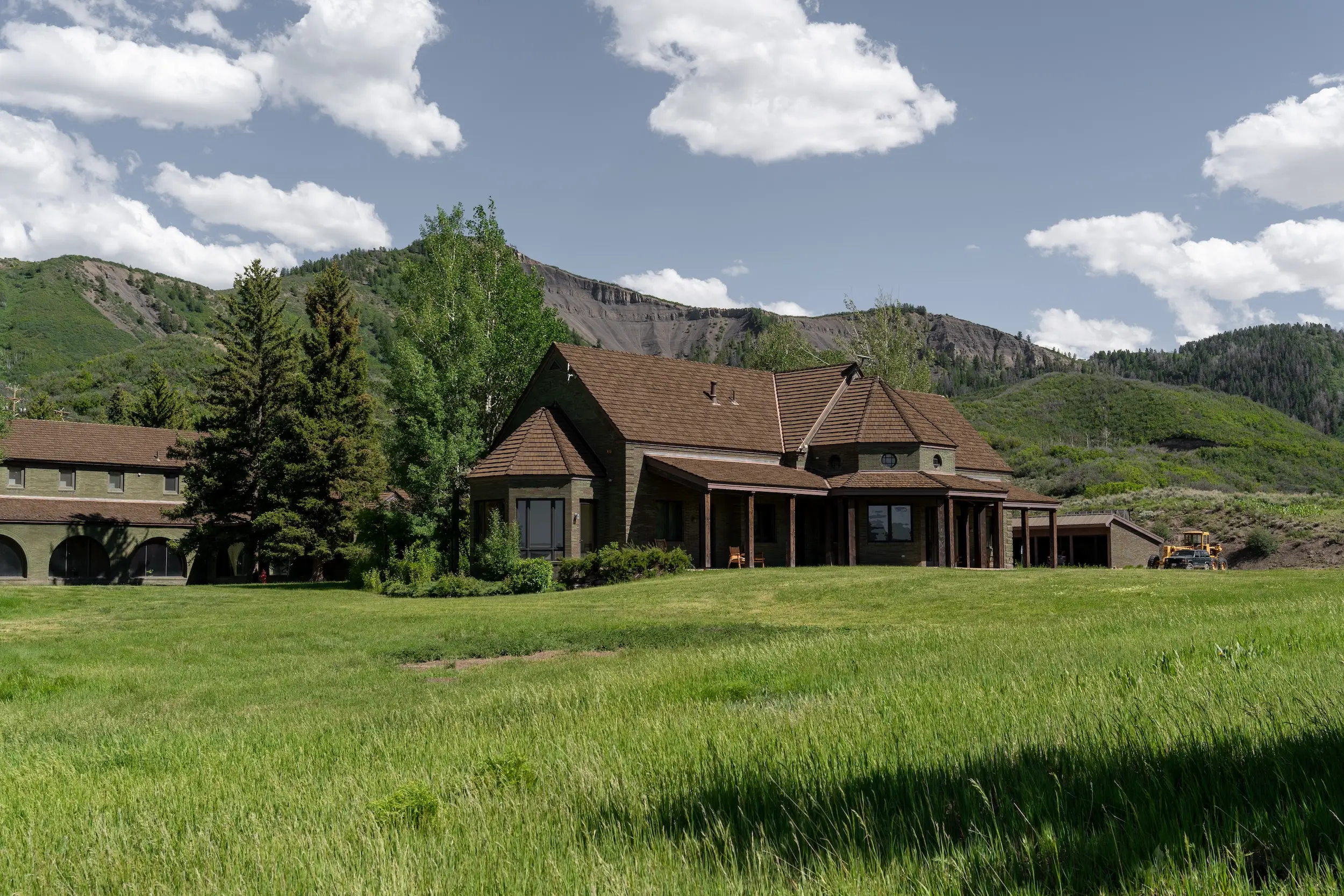 A building in a grassy field with a blue sky and mountains in the background.