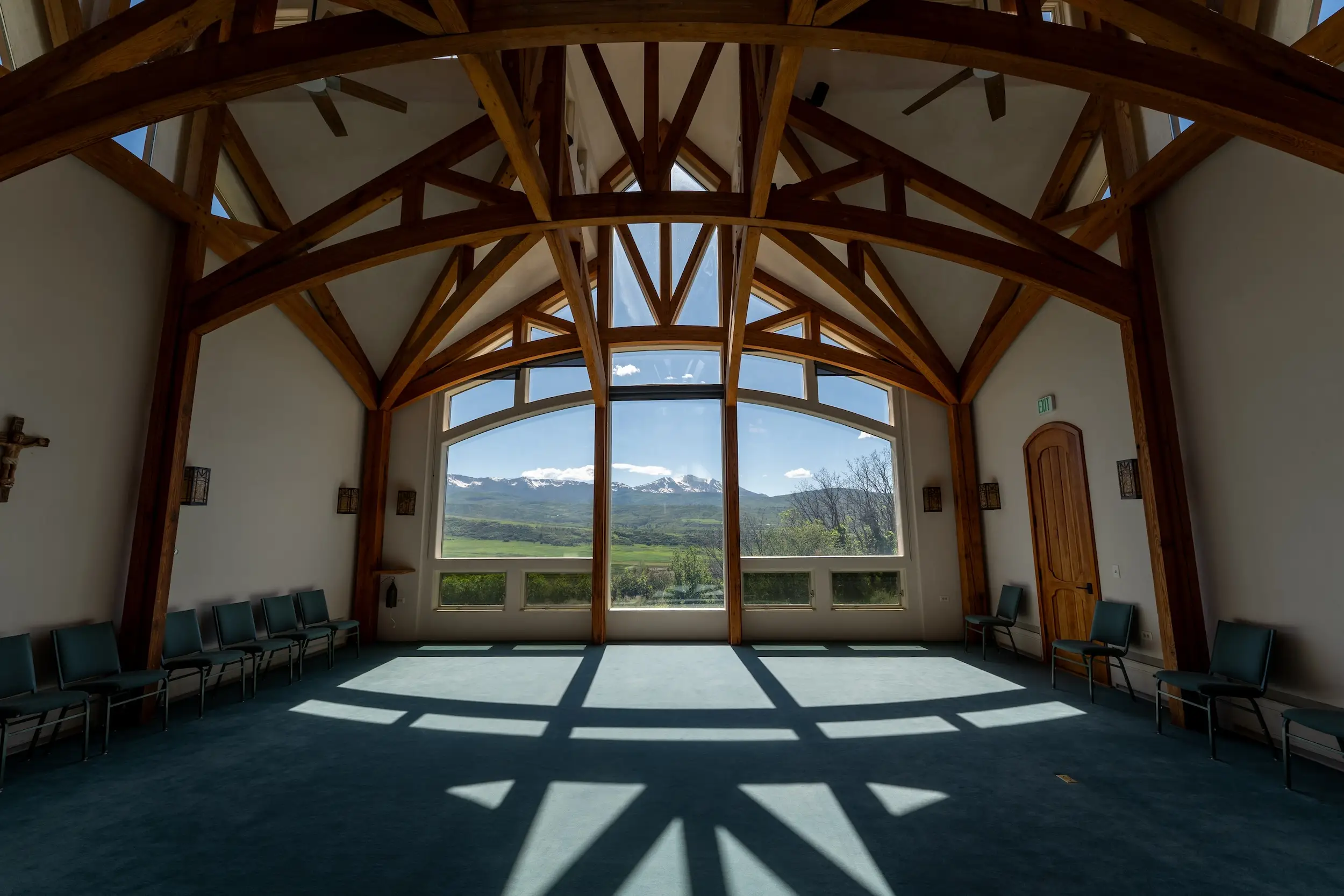 A room with several wooden beams across the ceiling and a large window taking up one of the walls with a view of mountains.