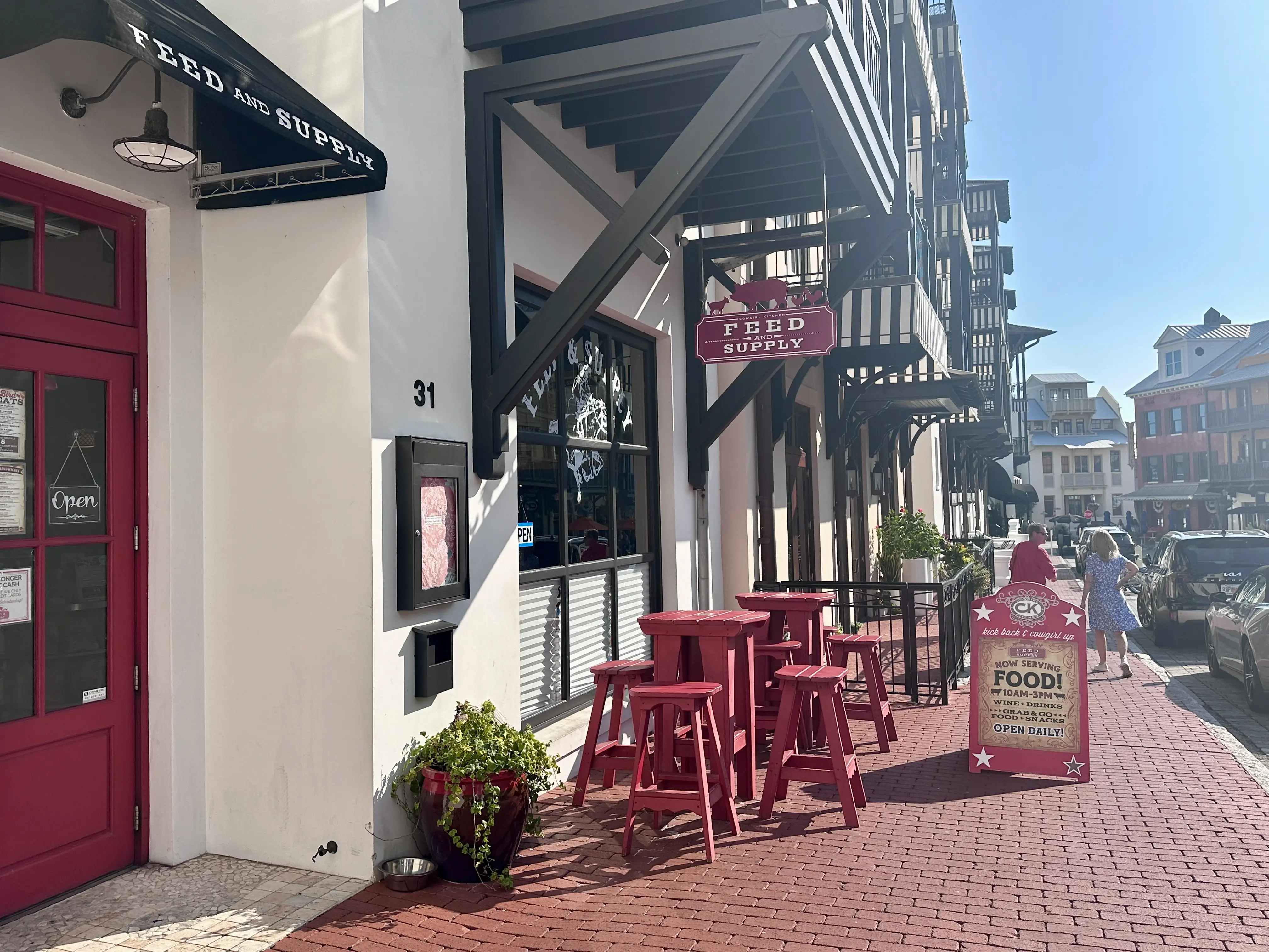 Red tables and chairs outside of a restaurant with brick sidewalks.