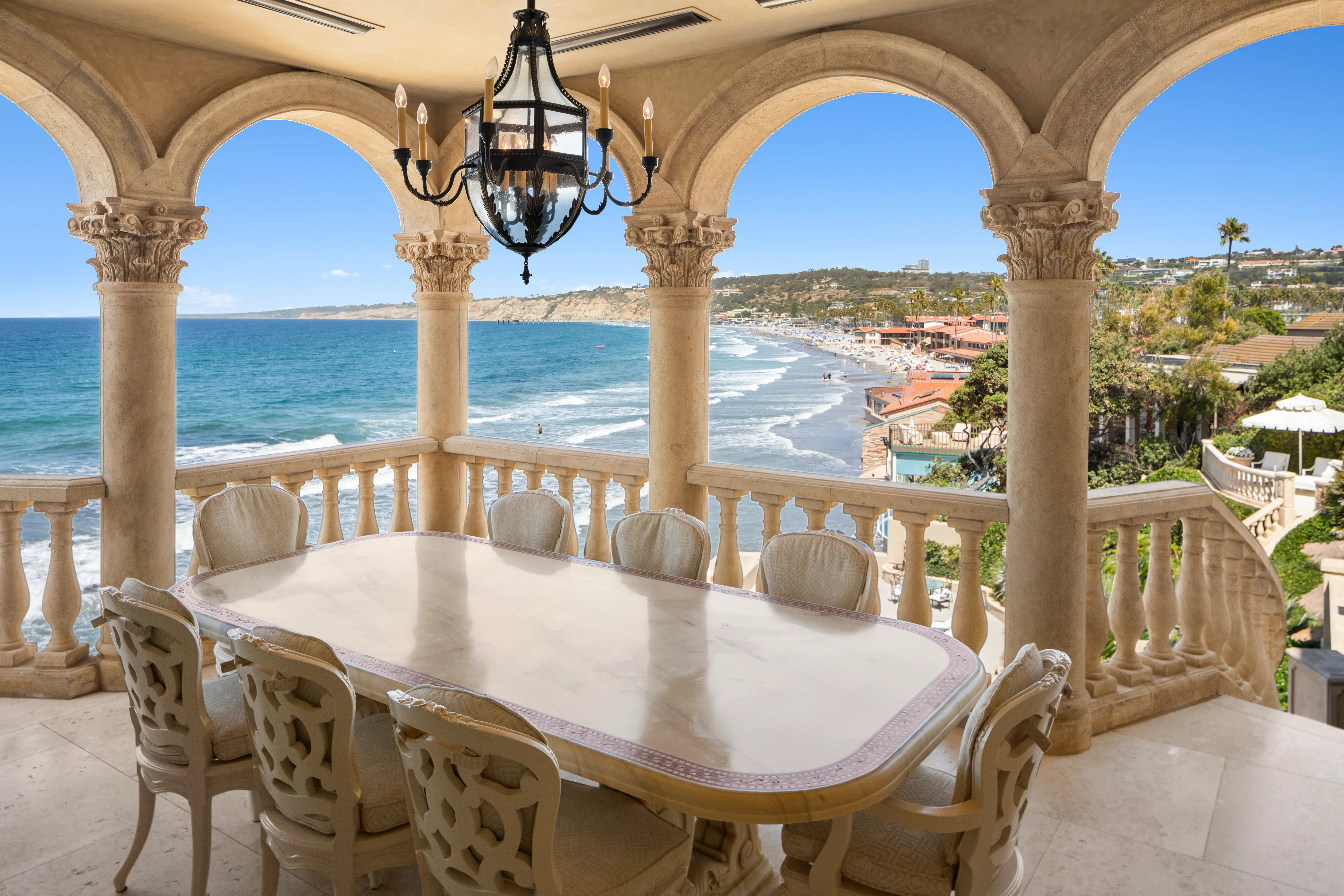 An outdoor dining area at the Sand Castle mansion, with a black chandelier and ocean view in the background.