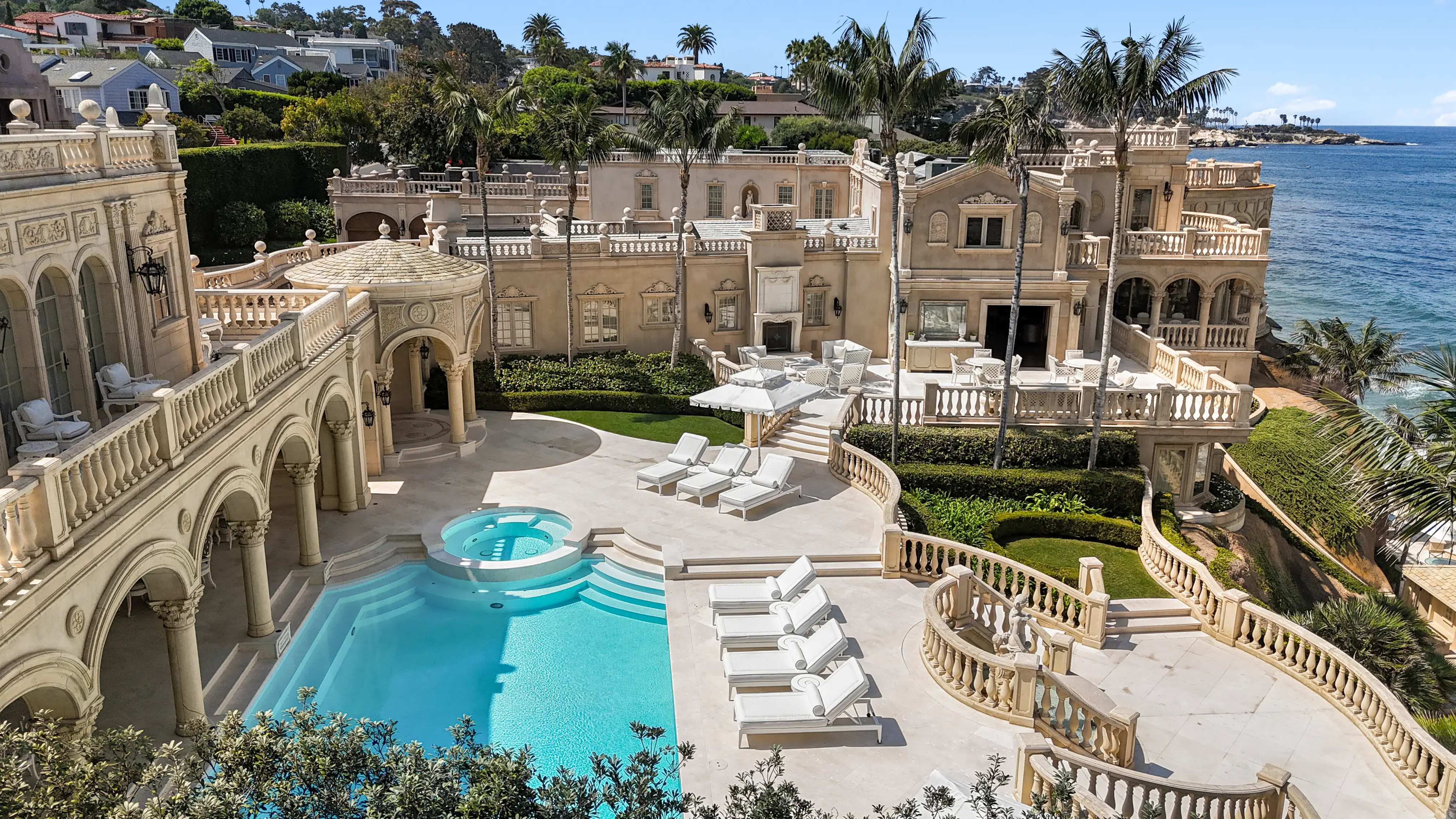 An overview of the Sand Castle backyard, featuring an elaborate pool, jacuzzi, white beach chairs, and an ocean view.