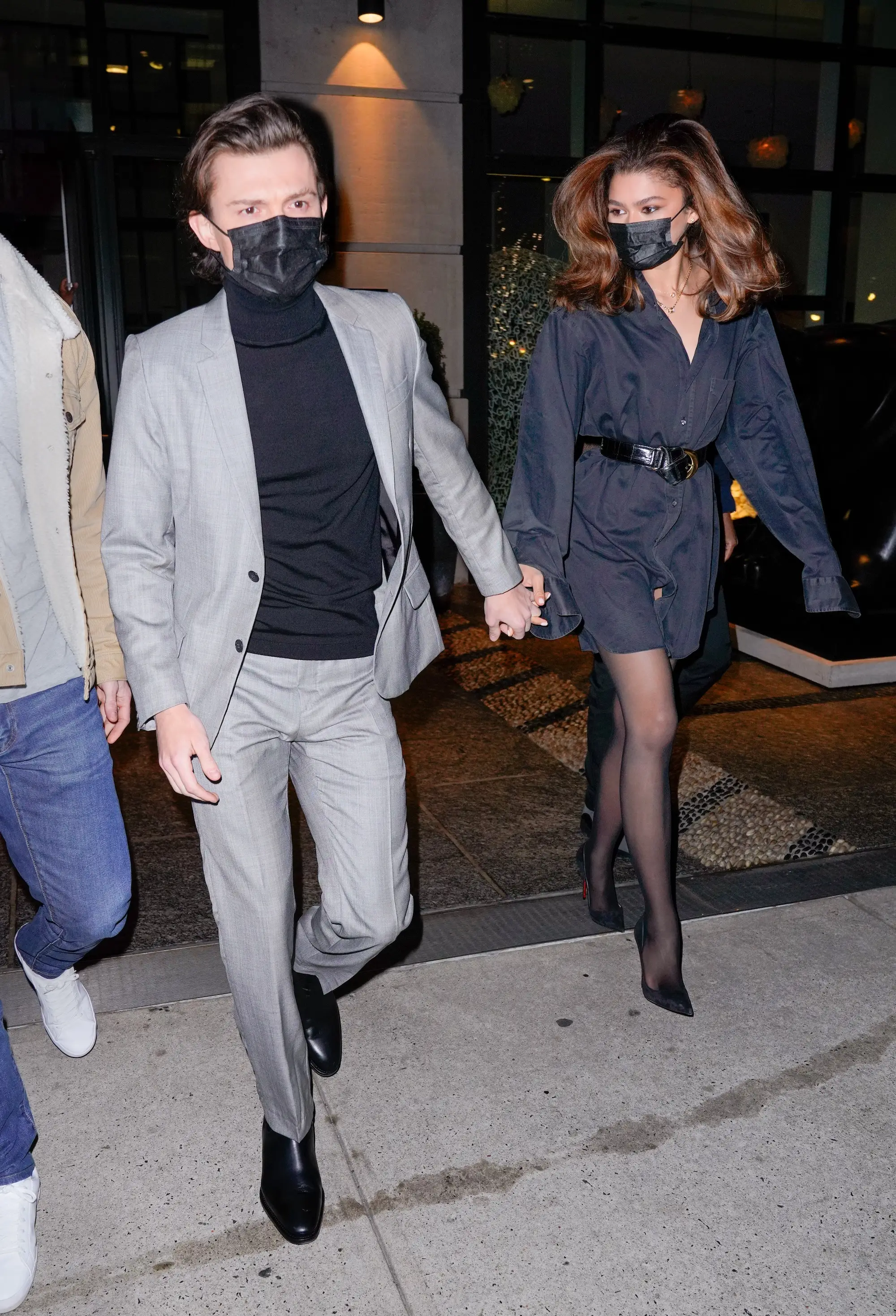 Zendaya and Tom Holland hold hands as they exit a building wearing masks.