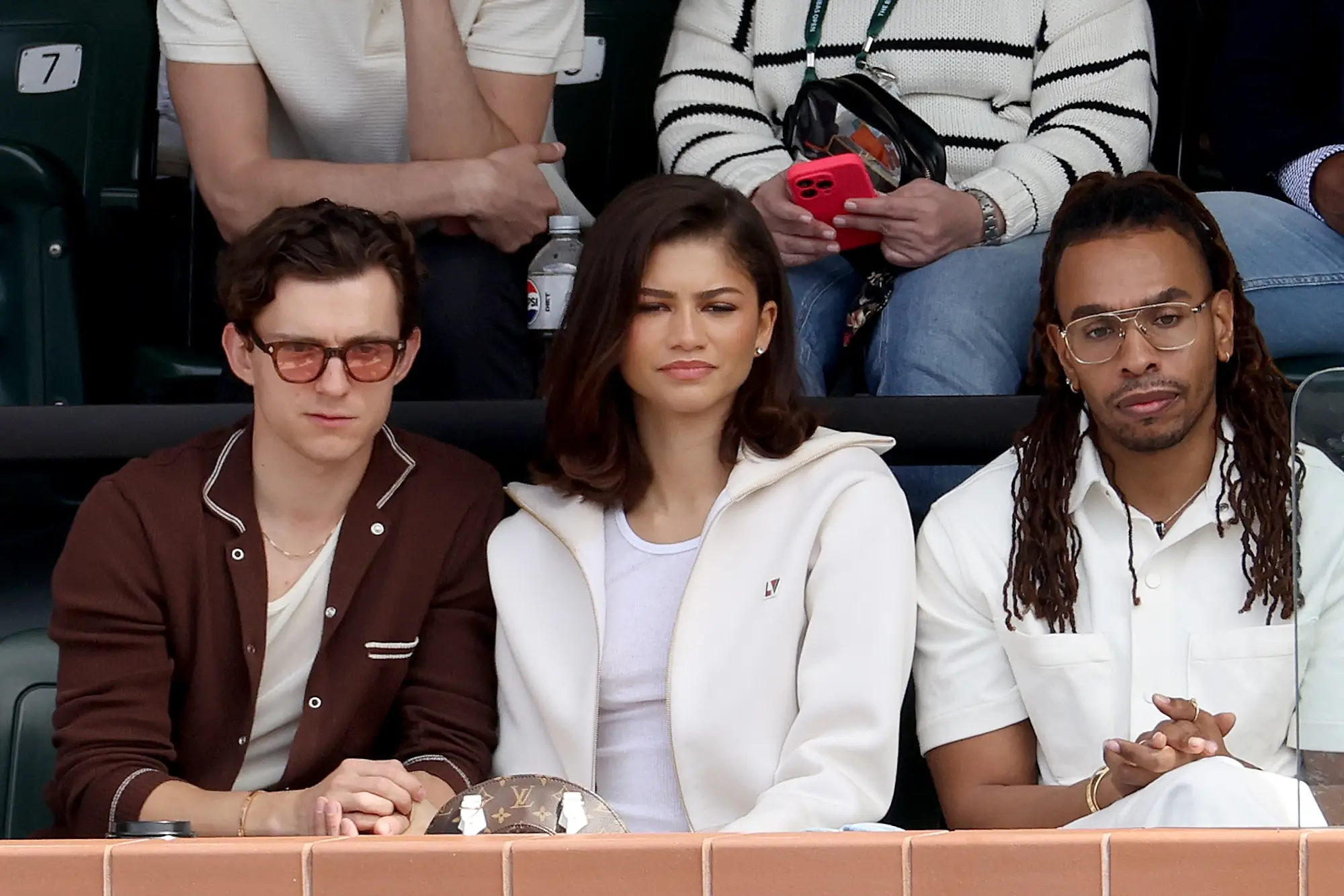 Zendaya and Tom Holland sit in the stands of a tennis match.