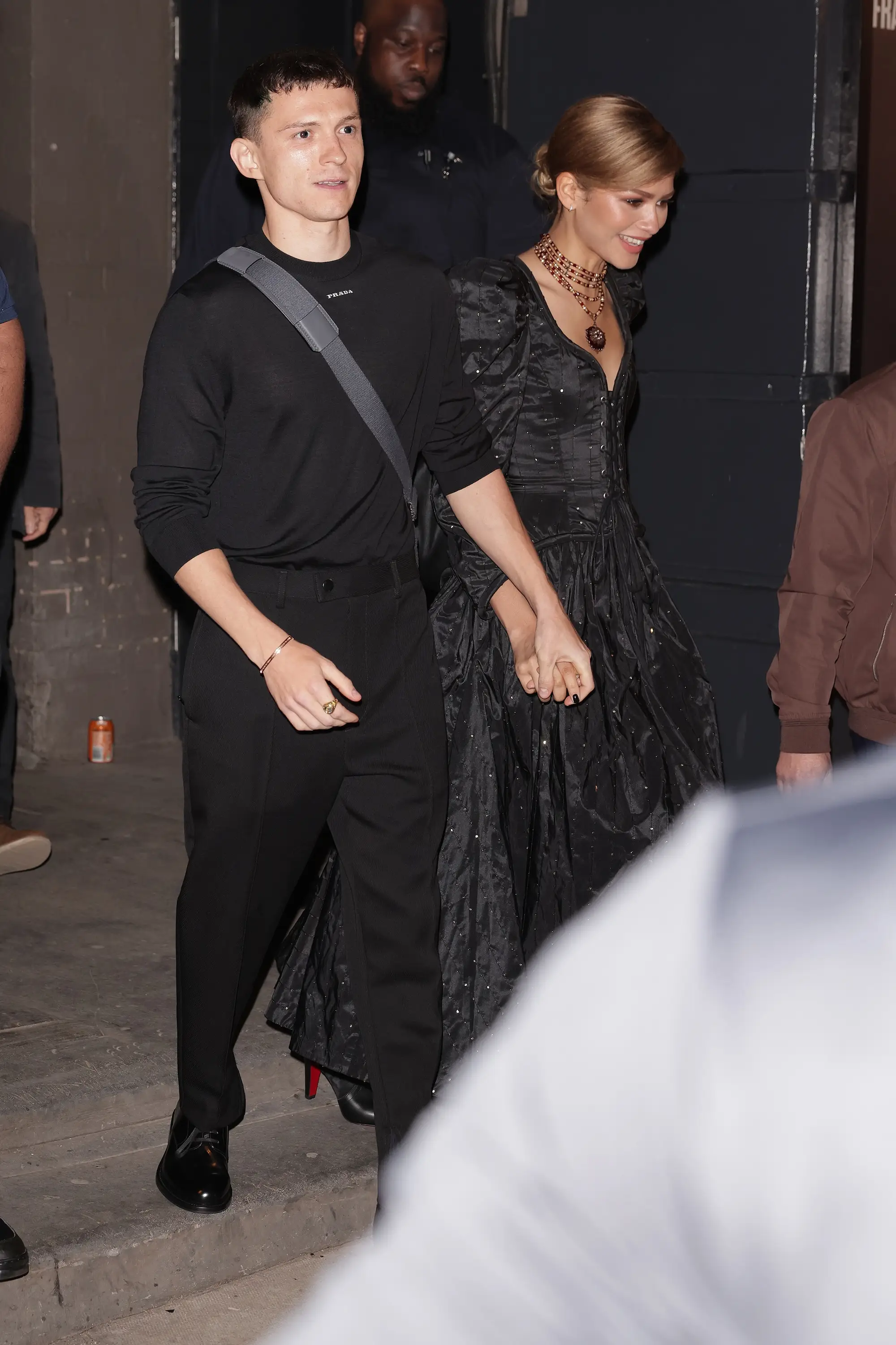 Tom Holland and Zendaya hold hands in black outfits.
