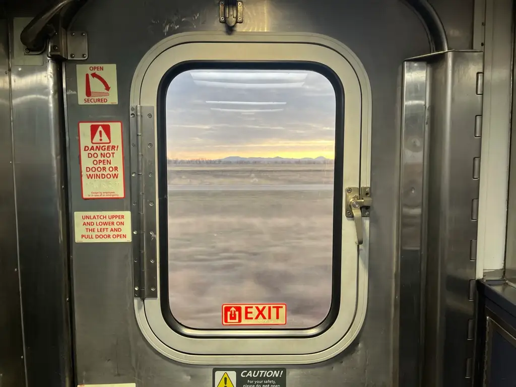 The exit door with a window on a moving Amtrak train at sunset.