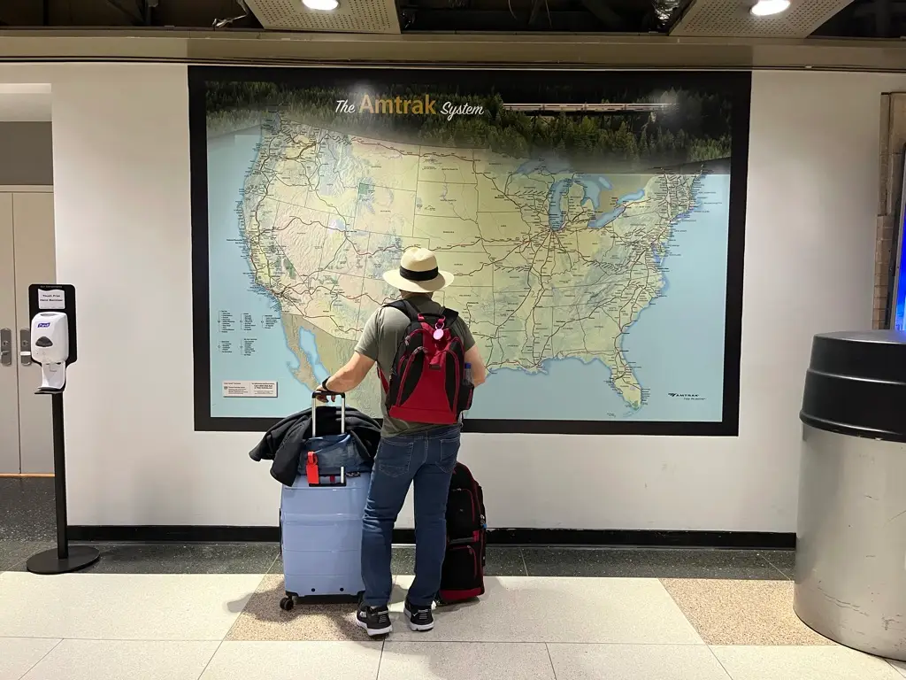 A man with luggage standing in front of a map with all the Amtrak routes.