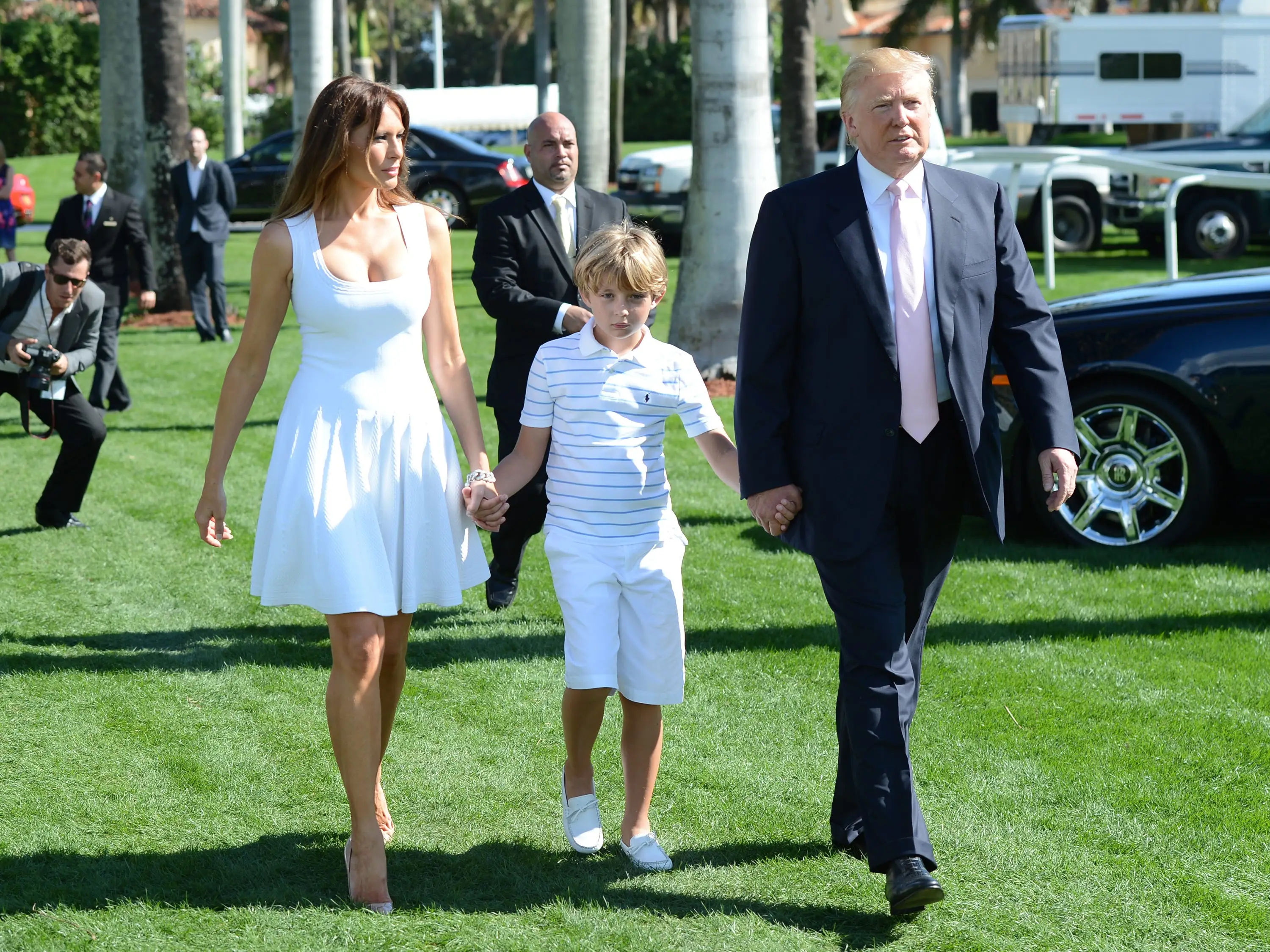 Melania Trump, Barron Trump, and Donald Trump walk across a golf course.