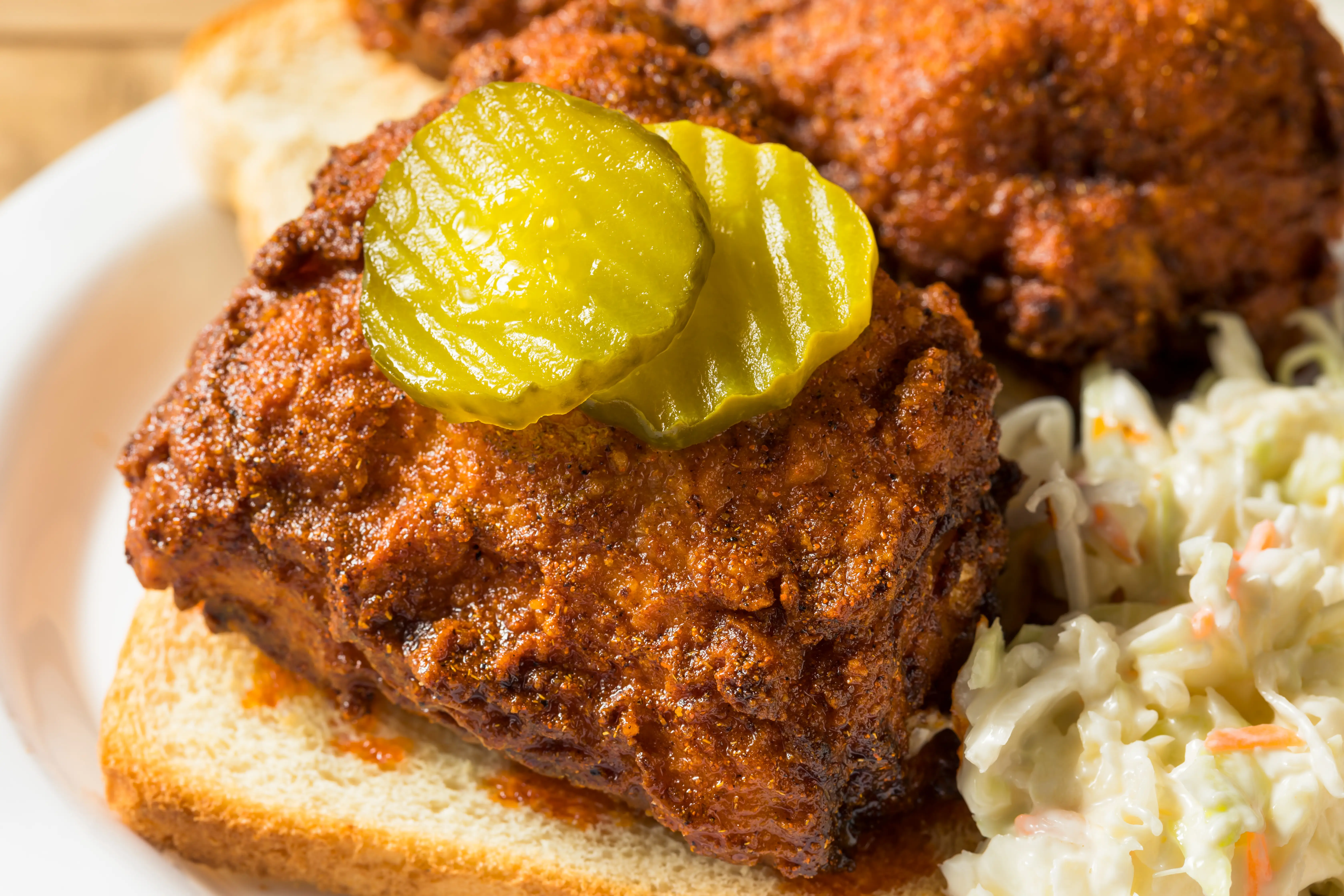 Nashville hot chicken with pickle slices on top next to coleslaw