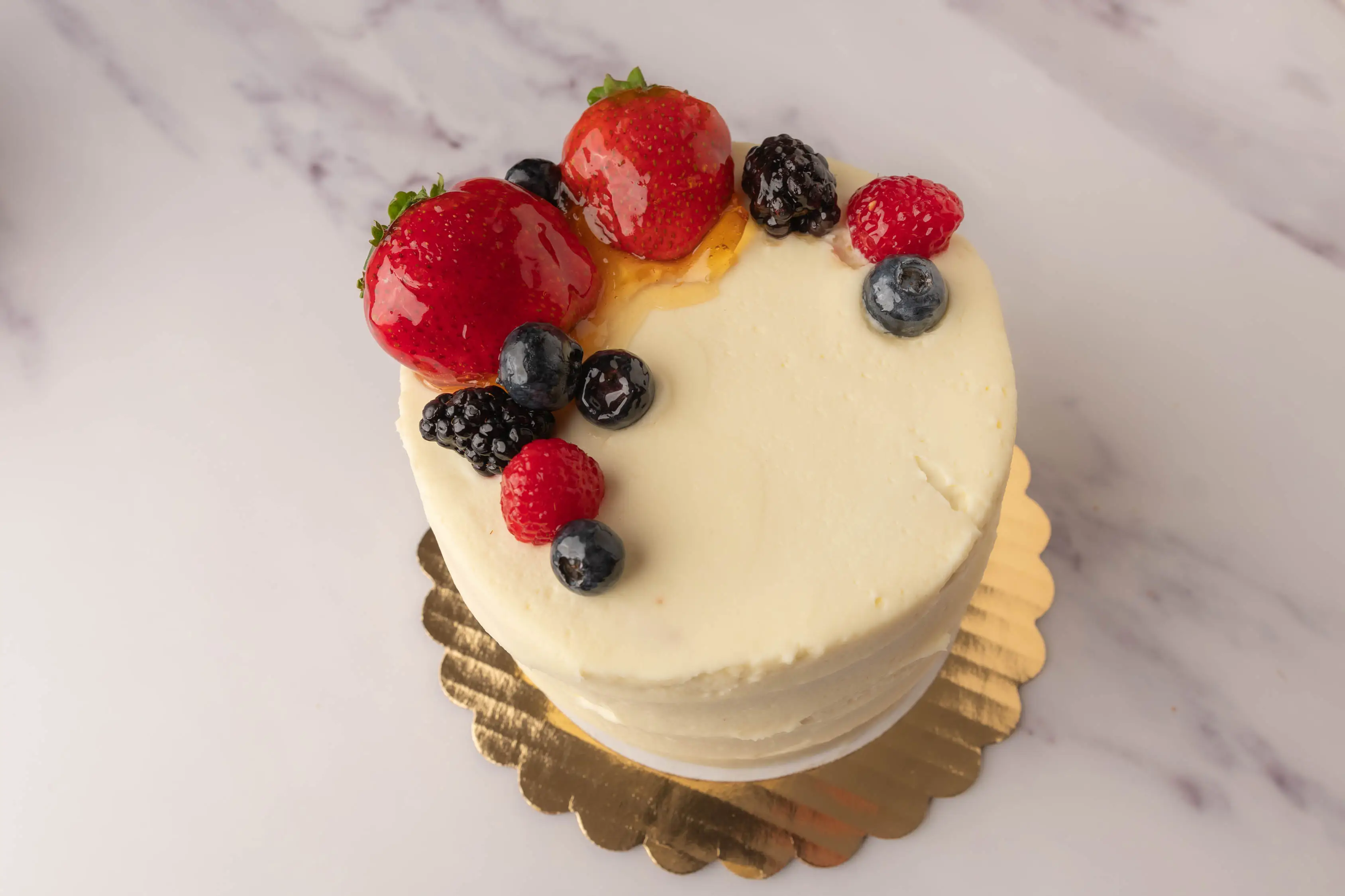 A Chantilly cake topped with strawberries, raspberries, blueberries, and blackberries on one side.