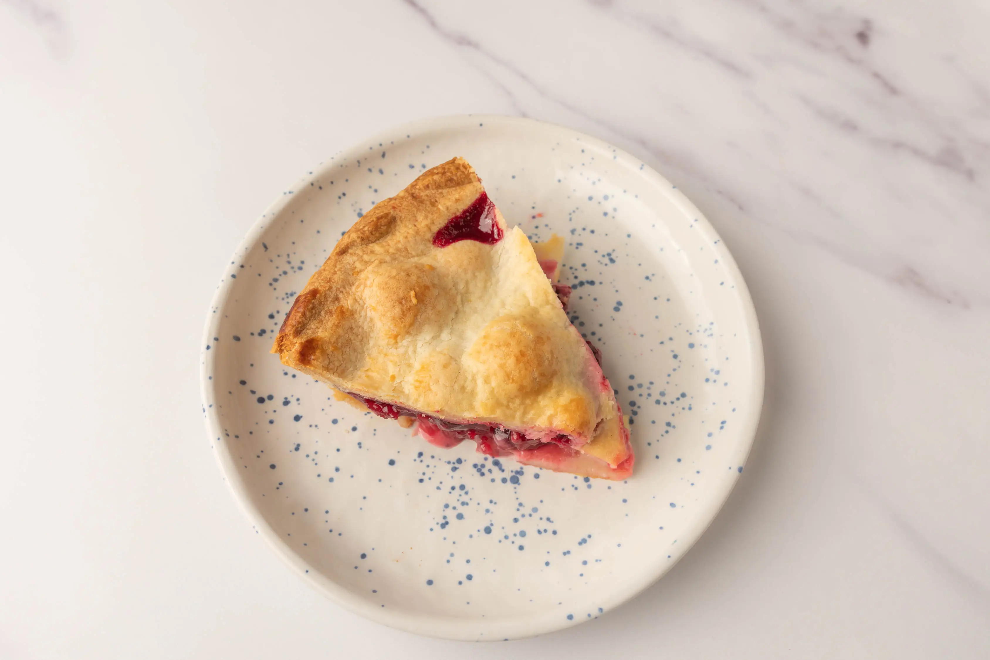 Slice of pie with golden crust on top and reddish filling from Wholefoods on white plate