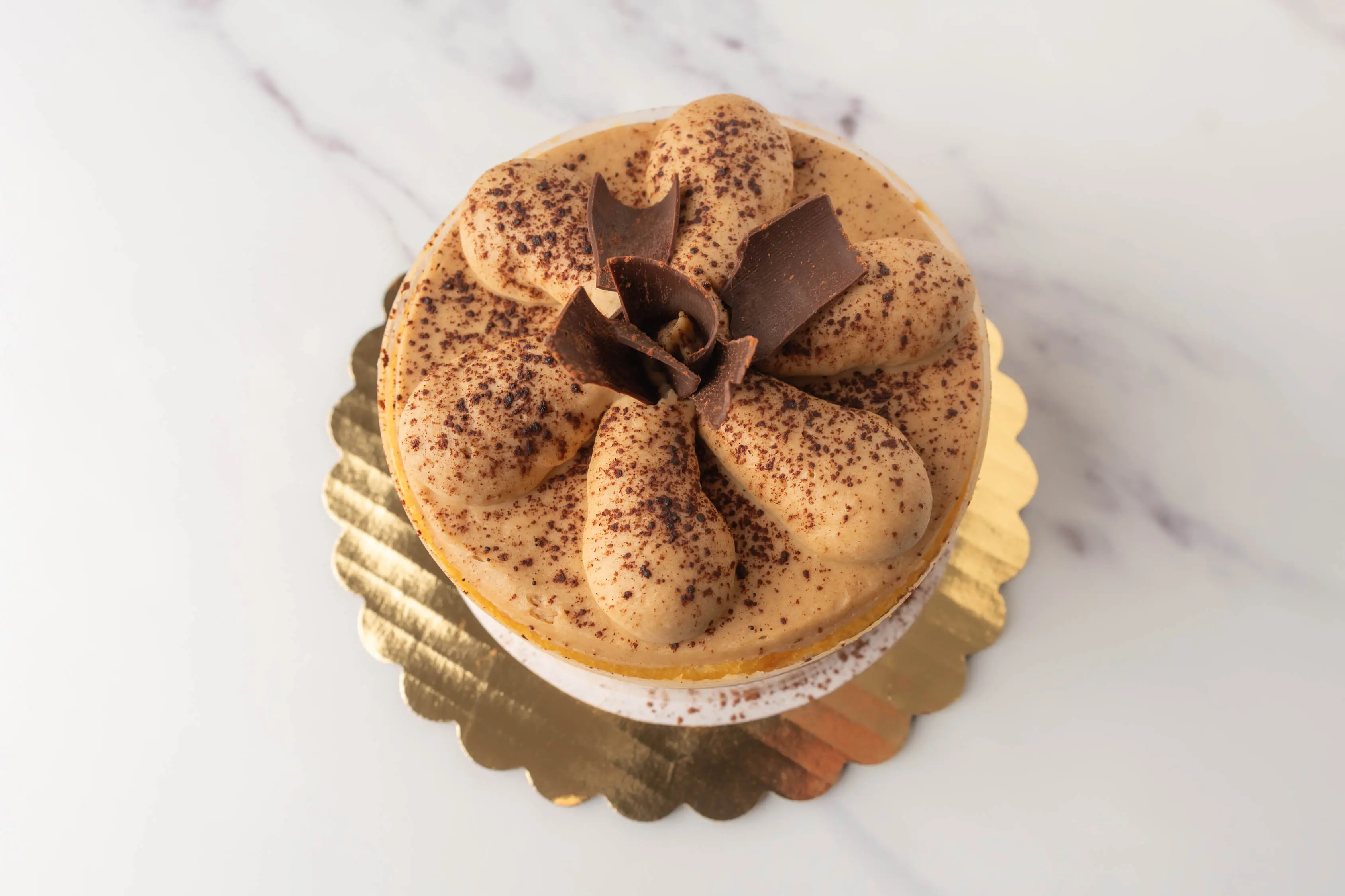 Wholefoods tiramisu cake with gobs of frosting on top, chocolate curls, and cocoa powder