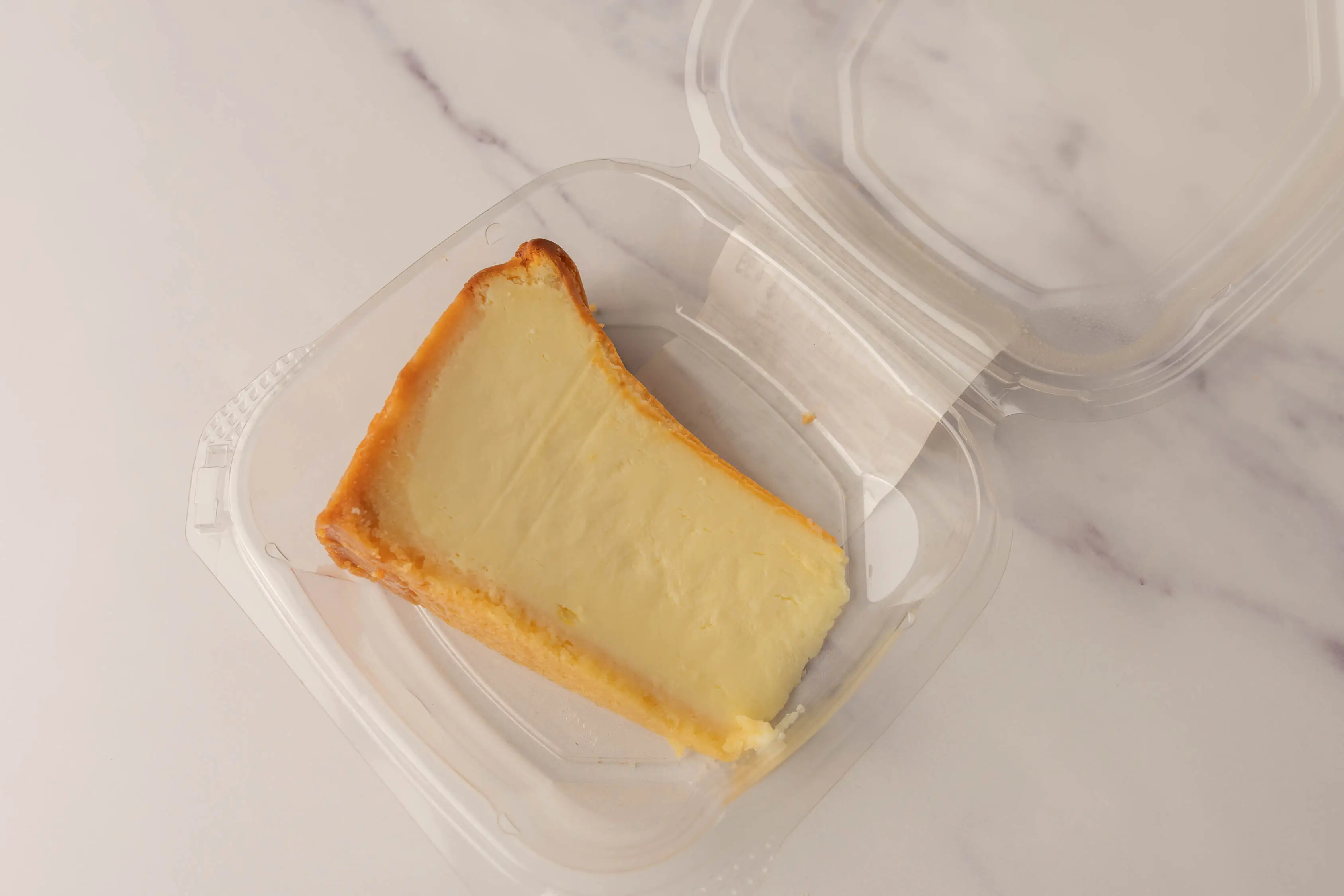 A baked cheesecake slice in a plastic clamshell package.