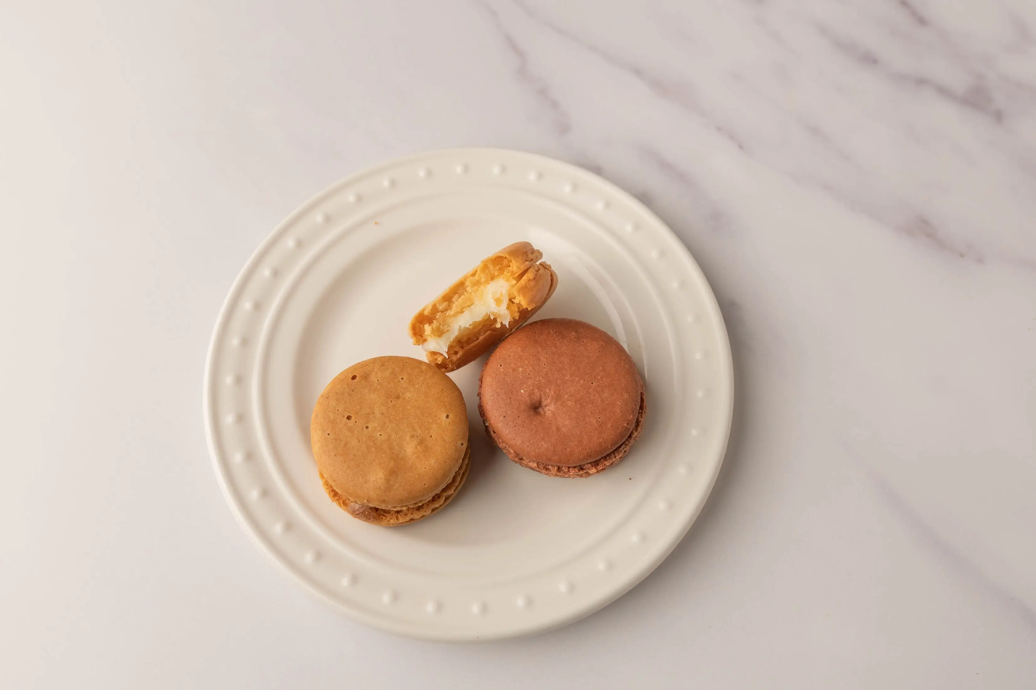 Three macarons on white plate, one with bite taken out of it