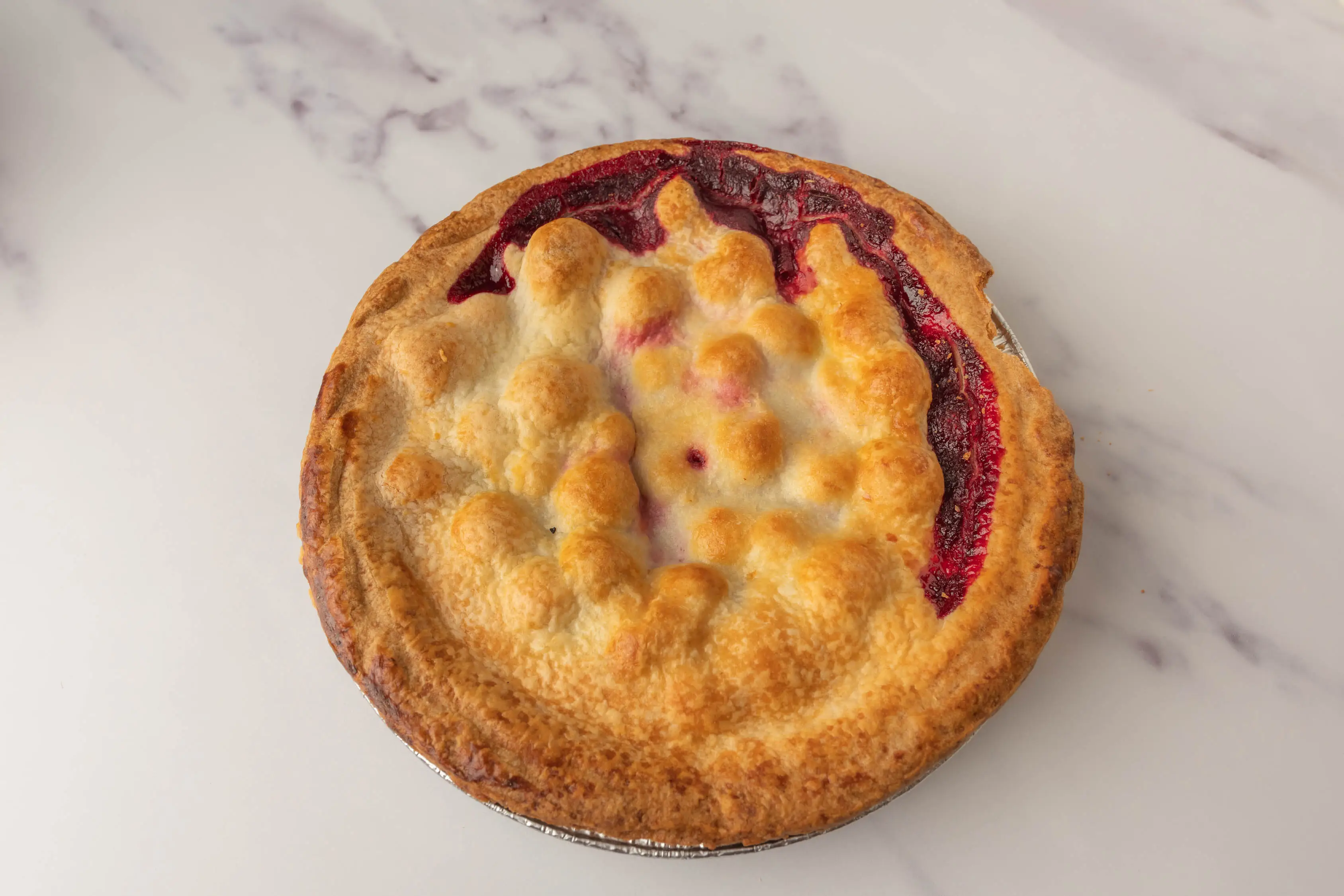 Pie with red filling peeking out from beneath golden crust from Wholefoods