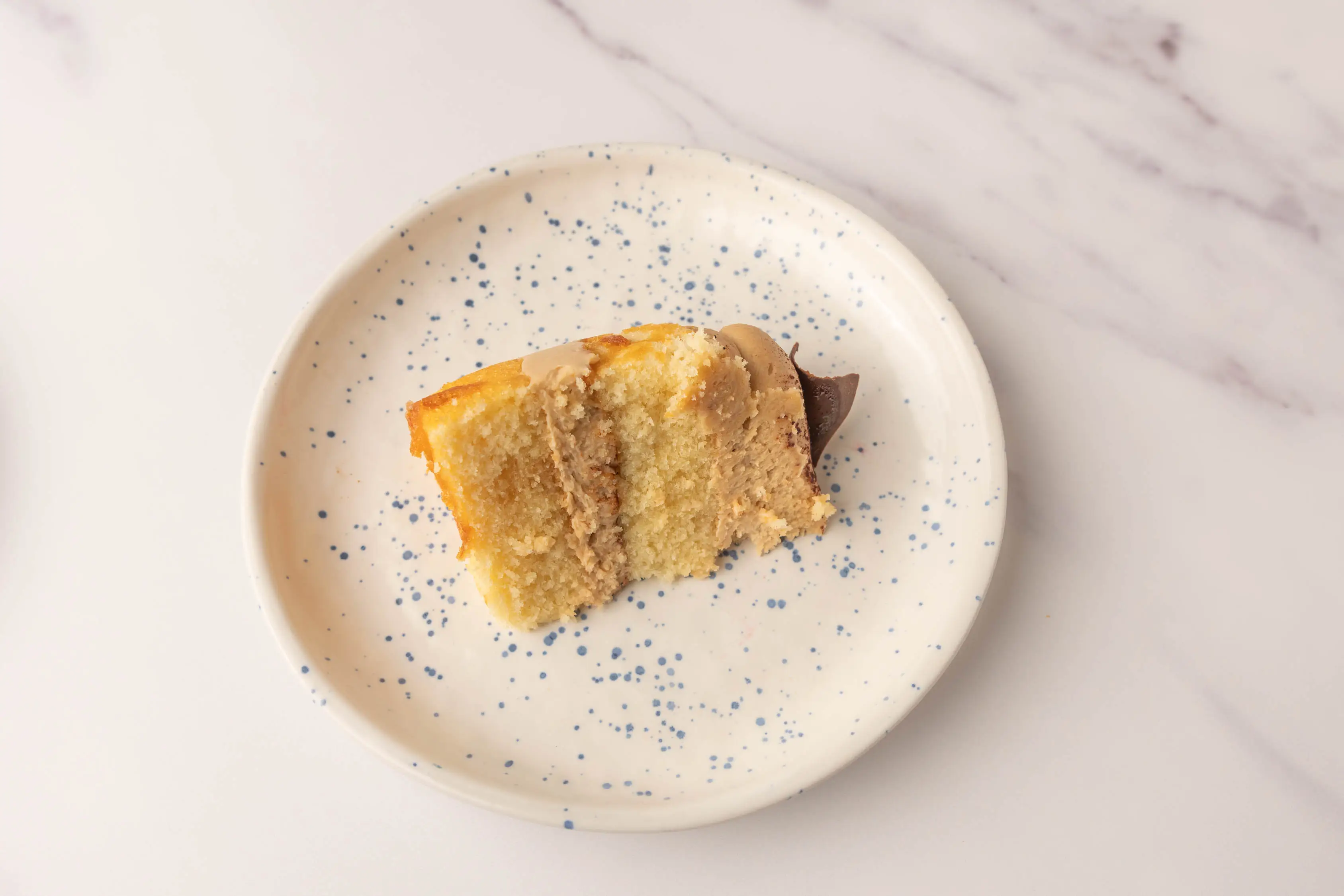 Slice of Wholefoods tiramisu cake with yellow cake and light-brown frosting on white plate