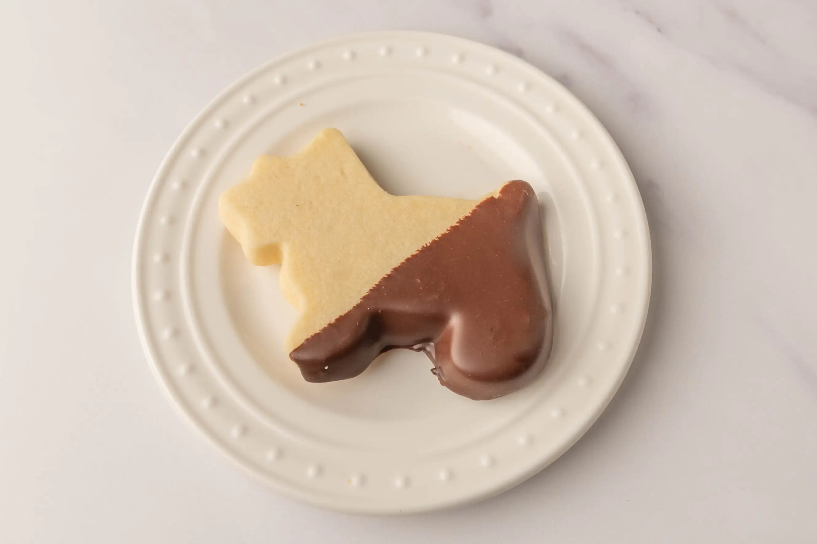 Dog-shaped shortbread cookie with bottom half dipped in chocolate from WholeFoods on white plate