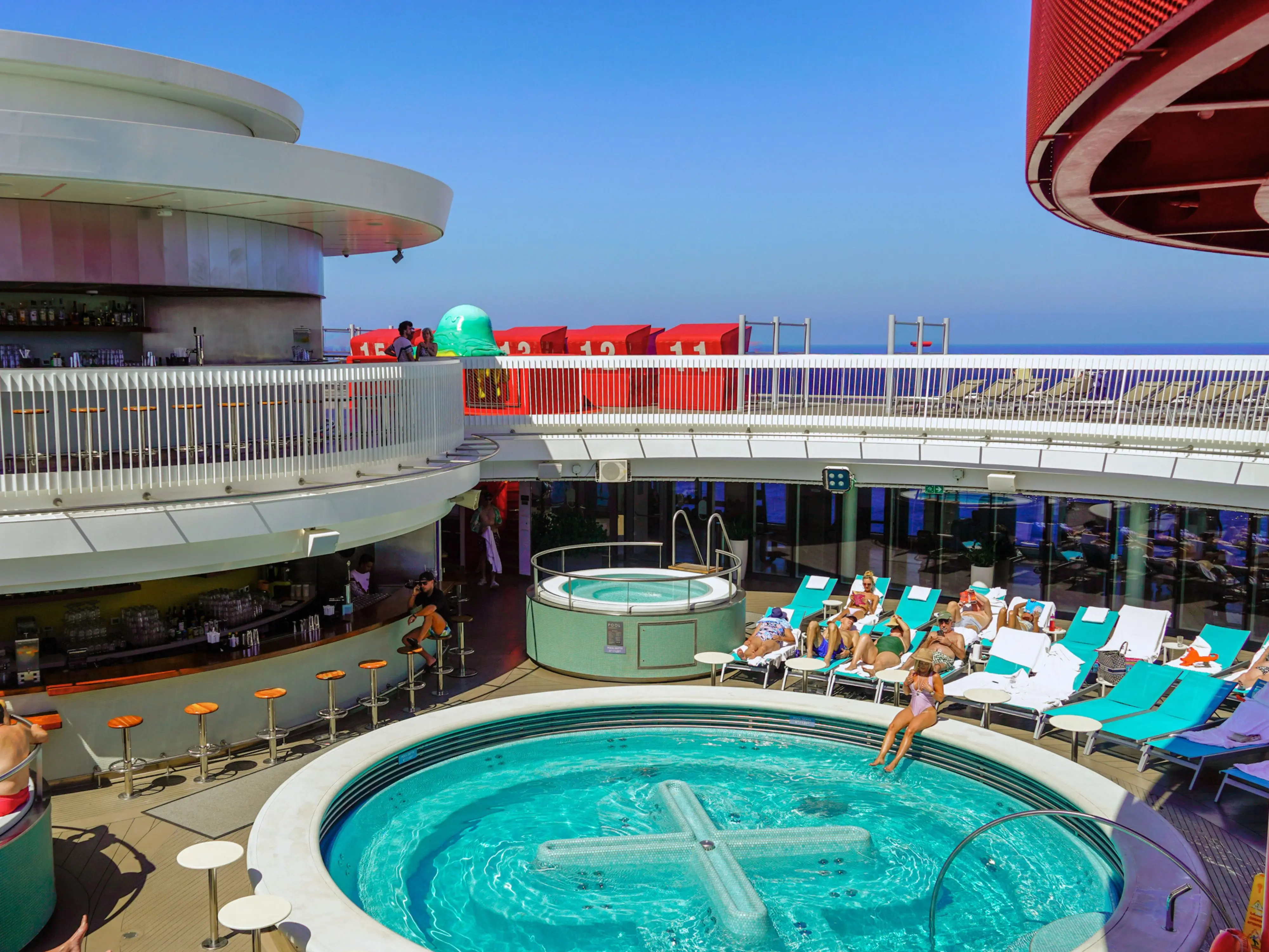 A pool deck on a cruise ship with a large whirlpool on the right and a bar on the left