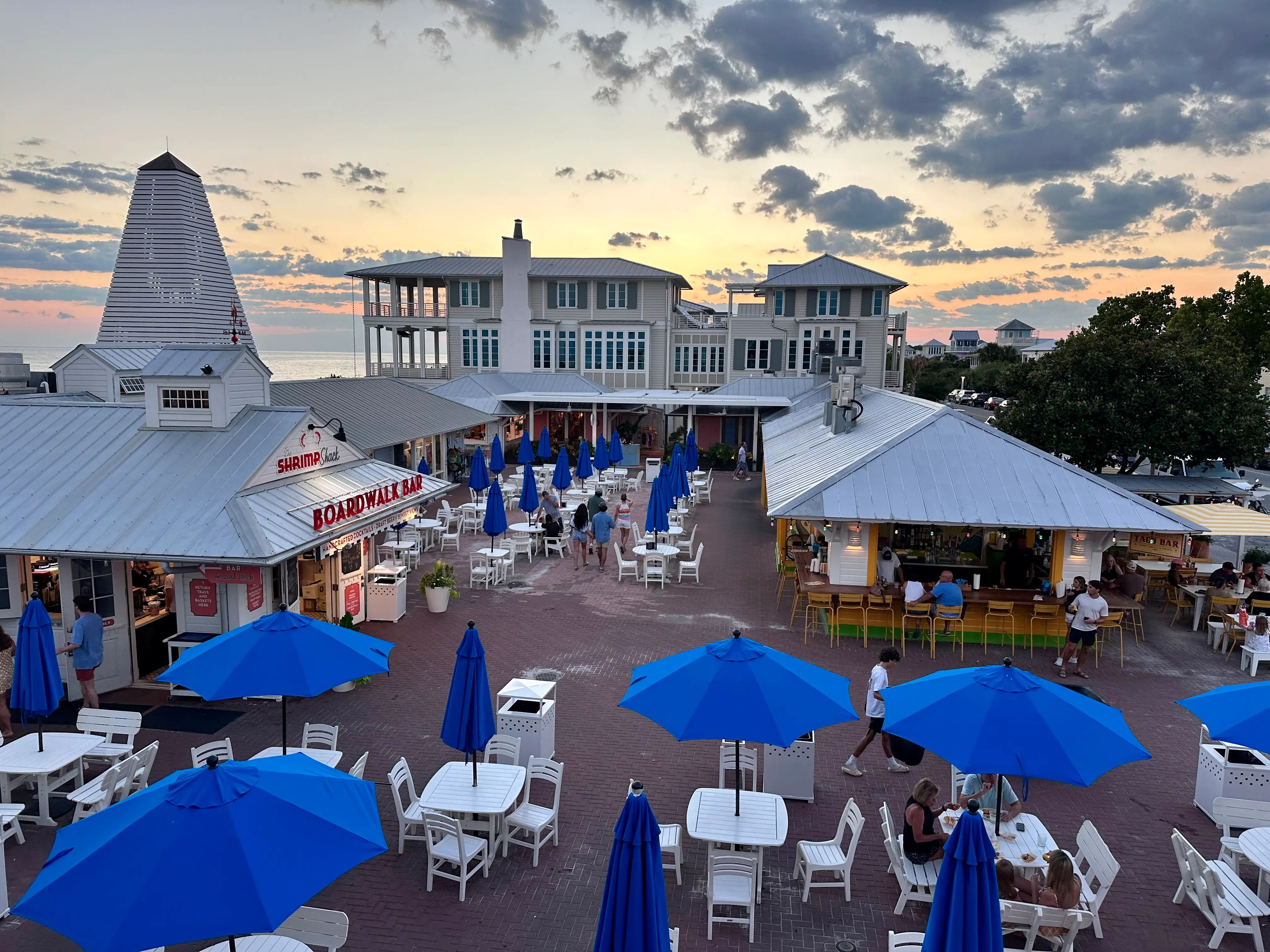 An above view of a boardwalk bar with tables and chairs at sunset.