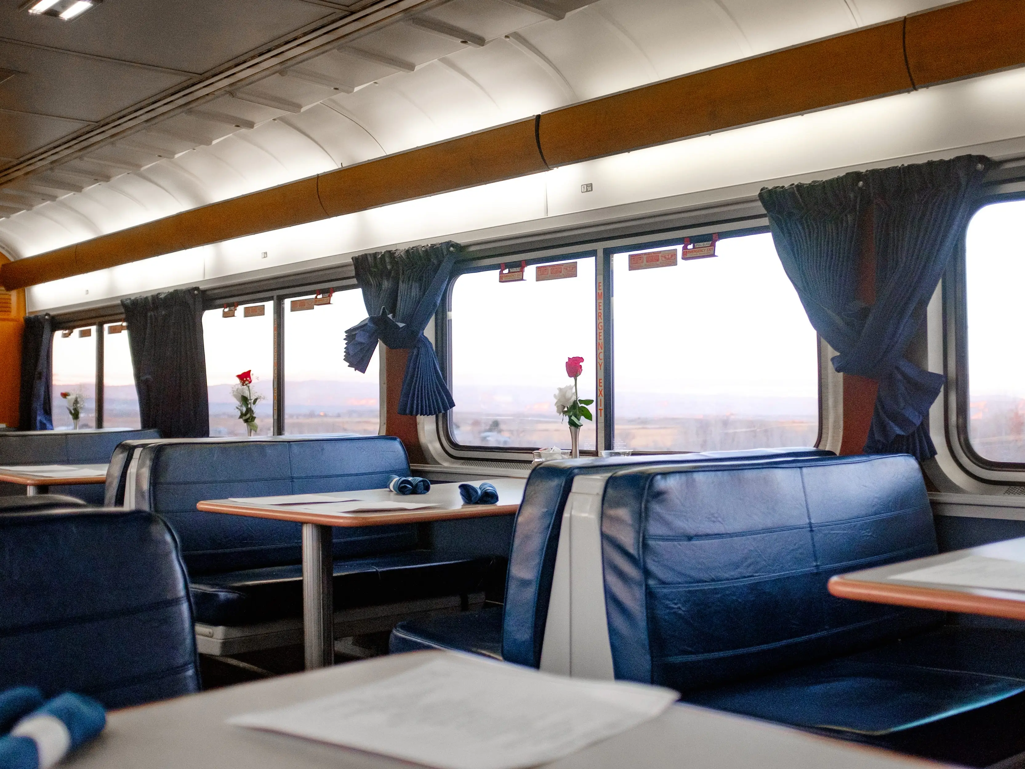 Inside a train dining car at sunset with red canyons out the window and booths with roses on them