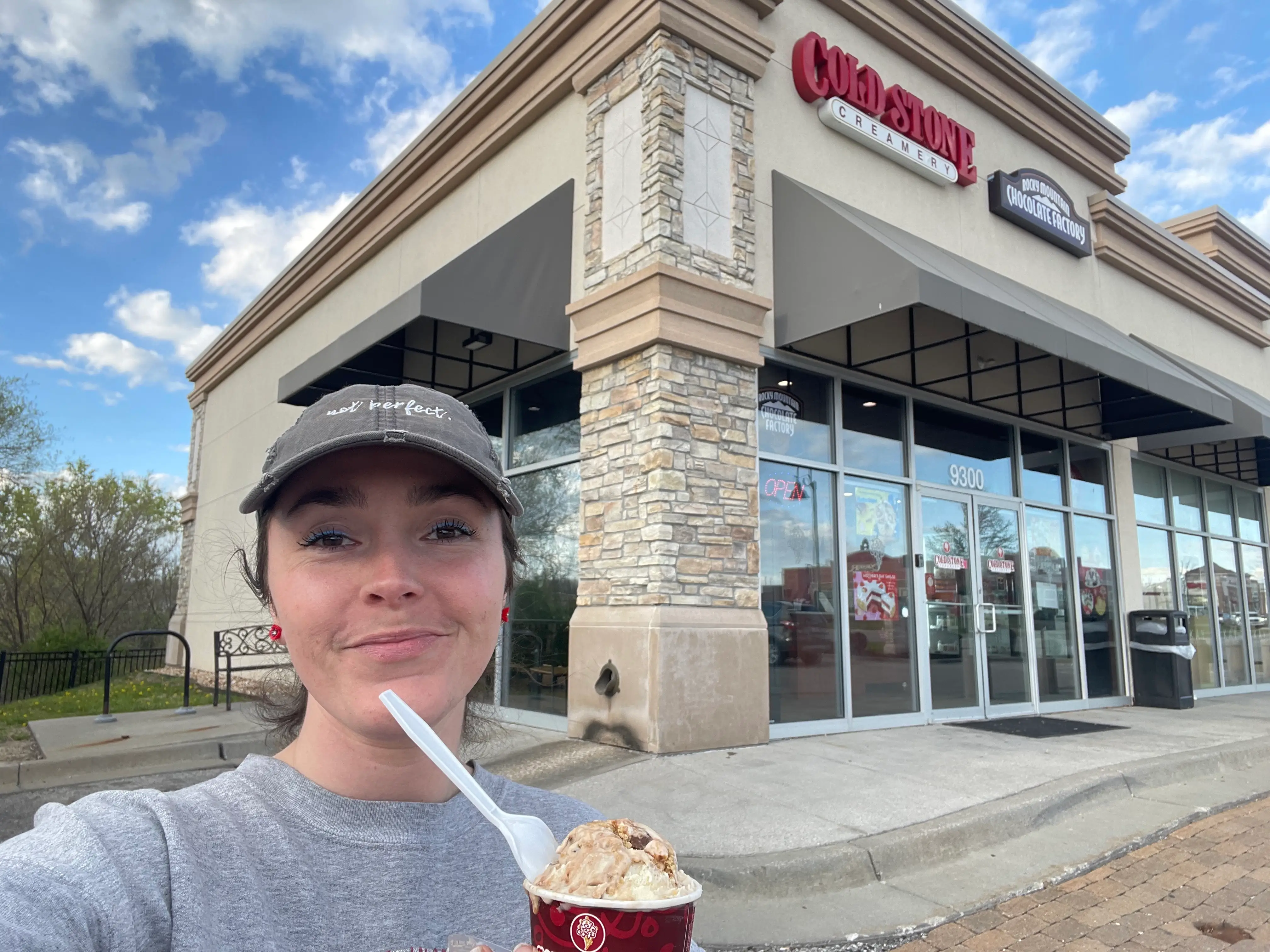 The author outside a Cold Stone Creamery wearing a hat and holding one of the cups of ice cream.