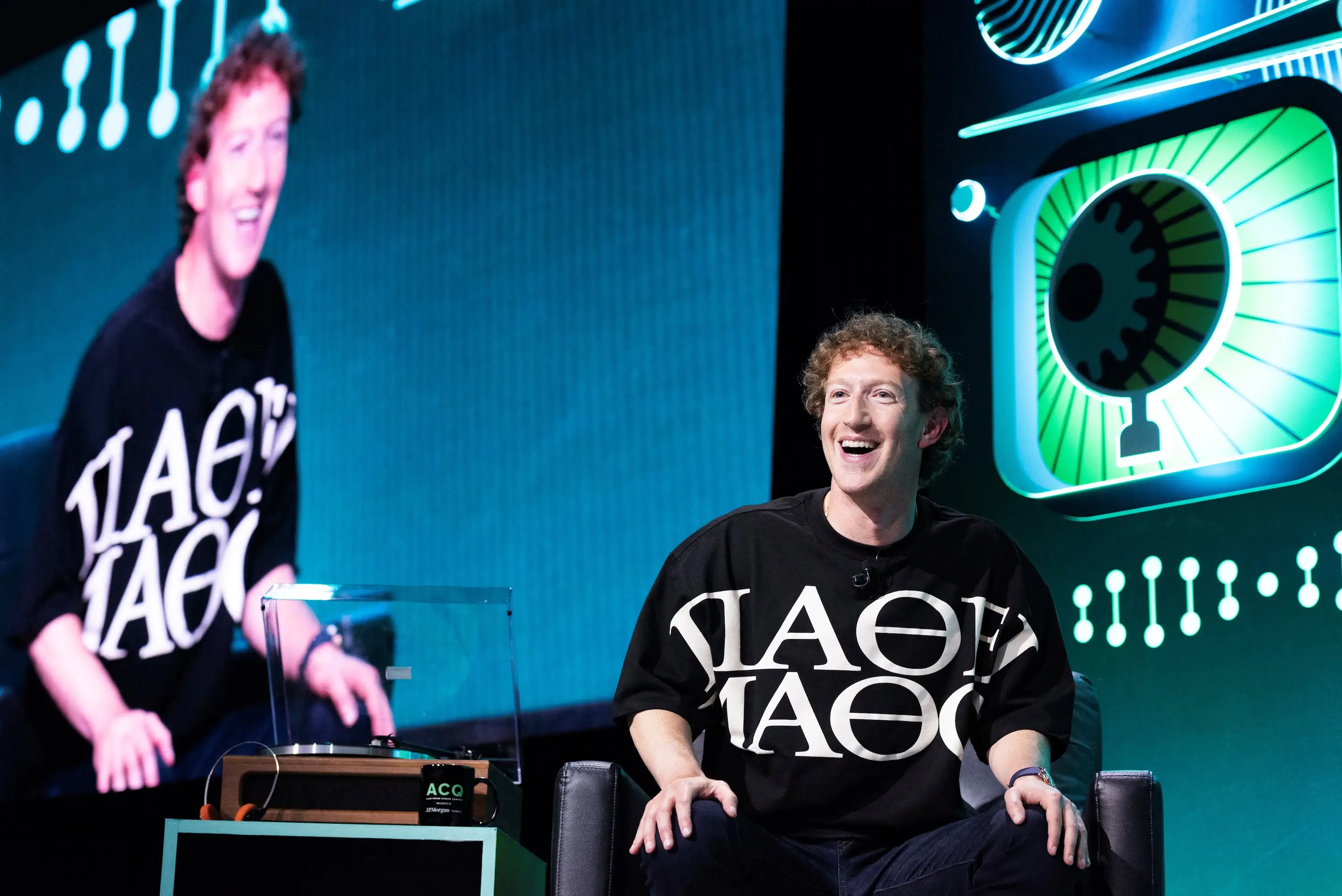 Mark Zuckerberg wears a graphic long-sleeved shirt and jeans while recording a live podcast.