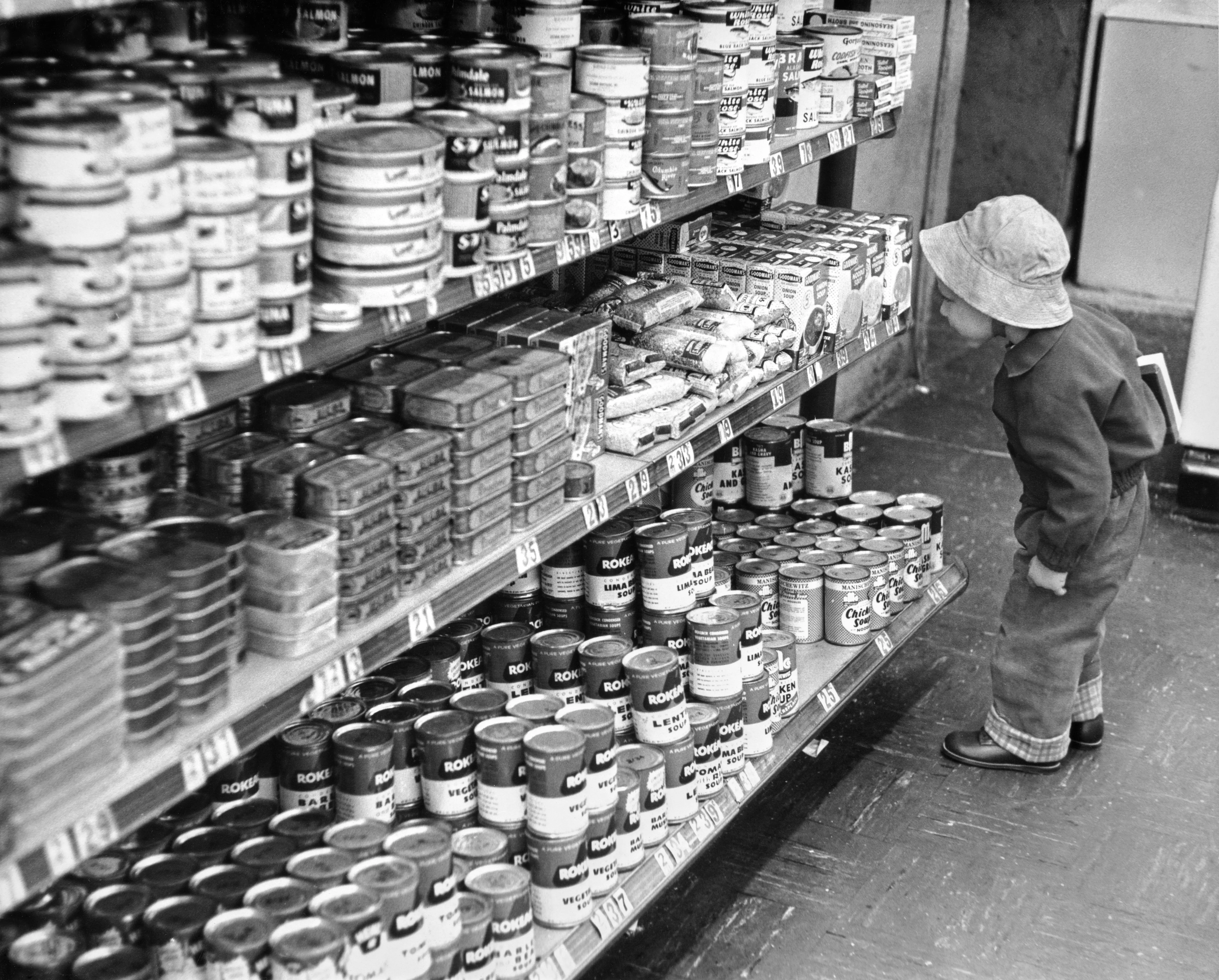 A child in a bucket hat looks at grocery store items on a shelf