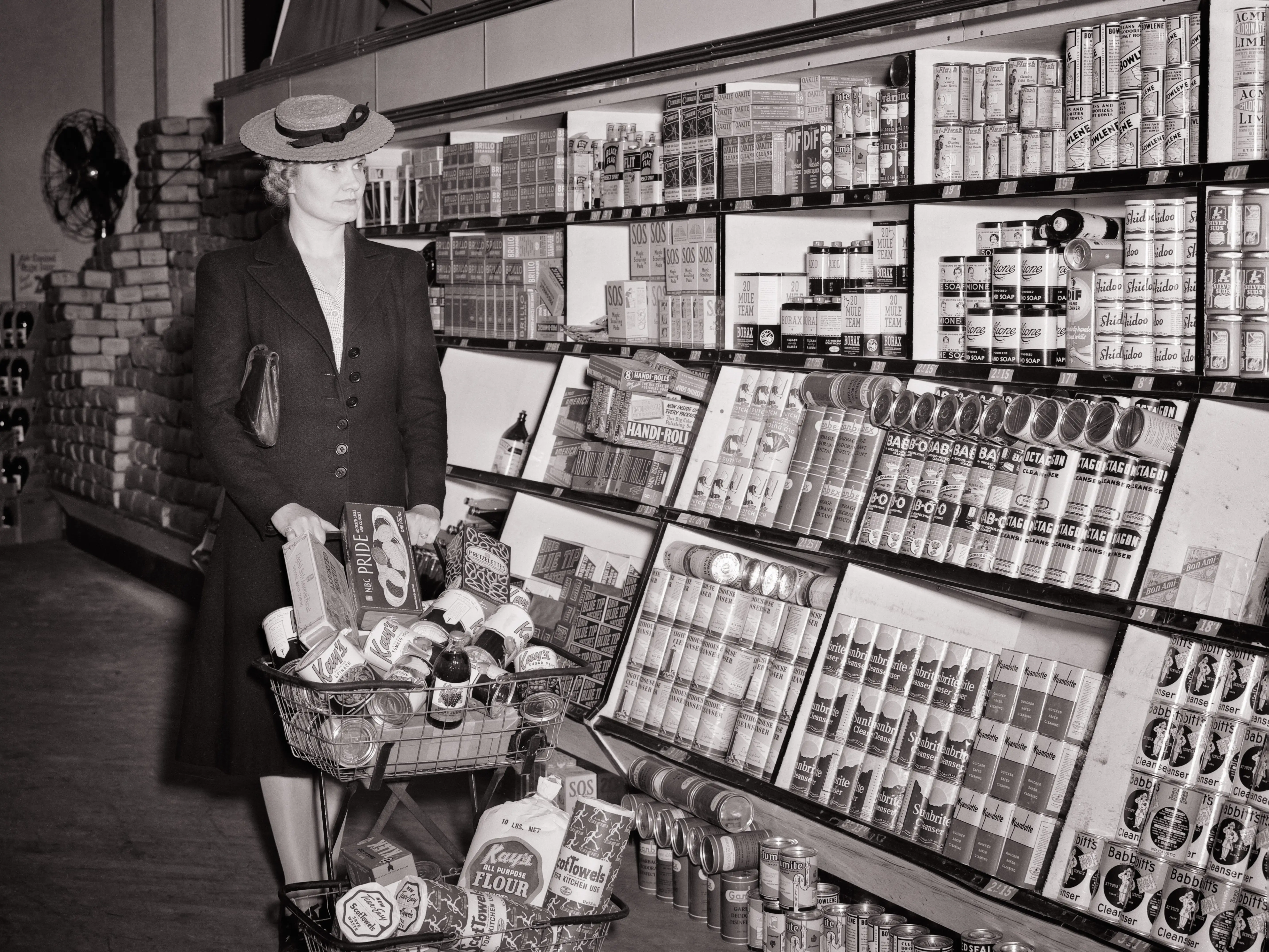 A woman looks at products on high shelves while pushing a full grocery cart