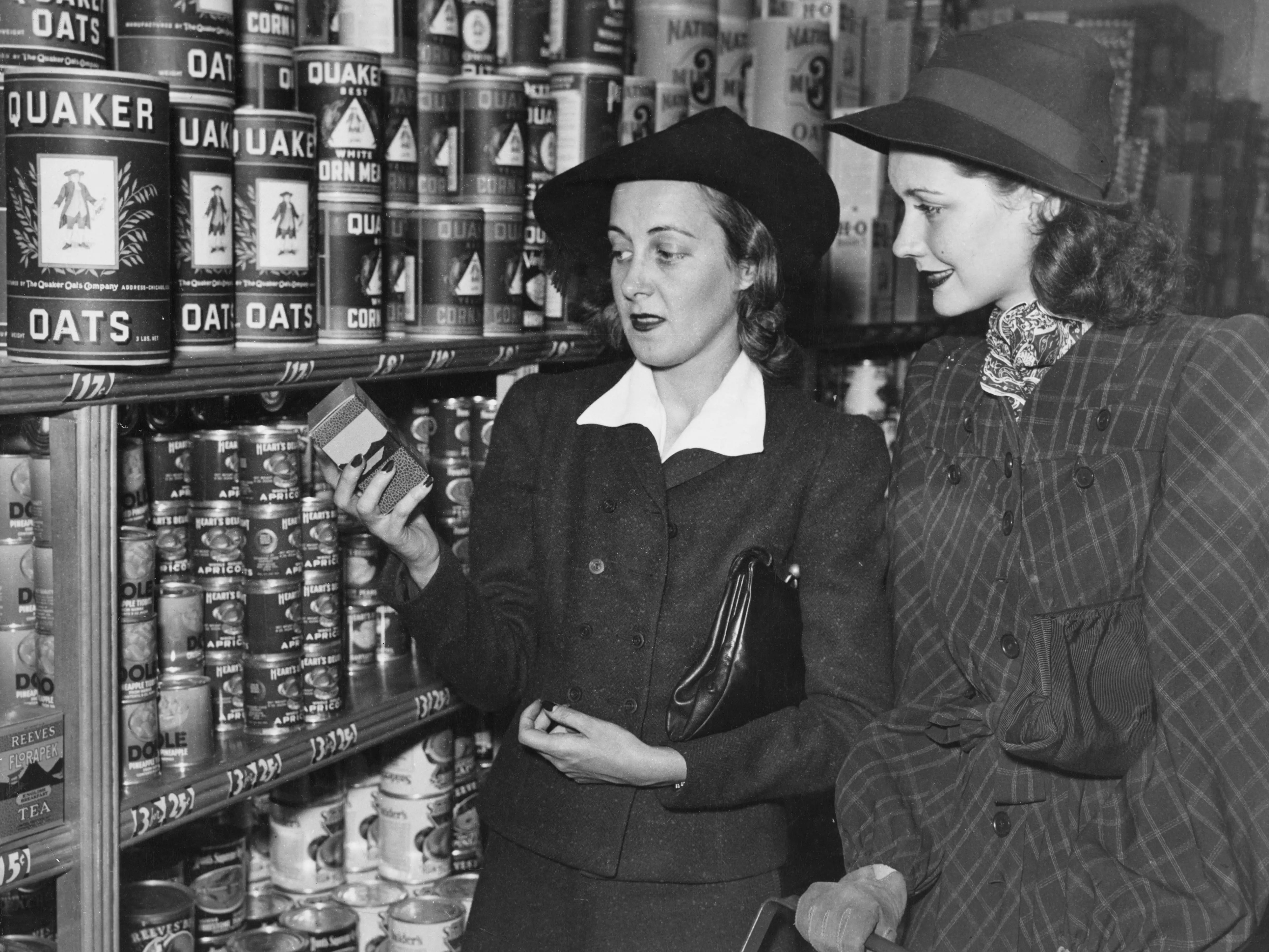Two woman in hats look at cans of Quaker Oats on a grocery store shelf