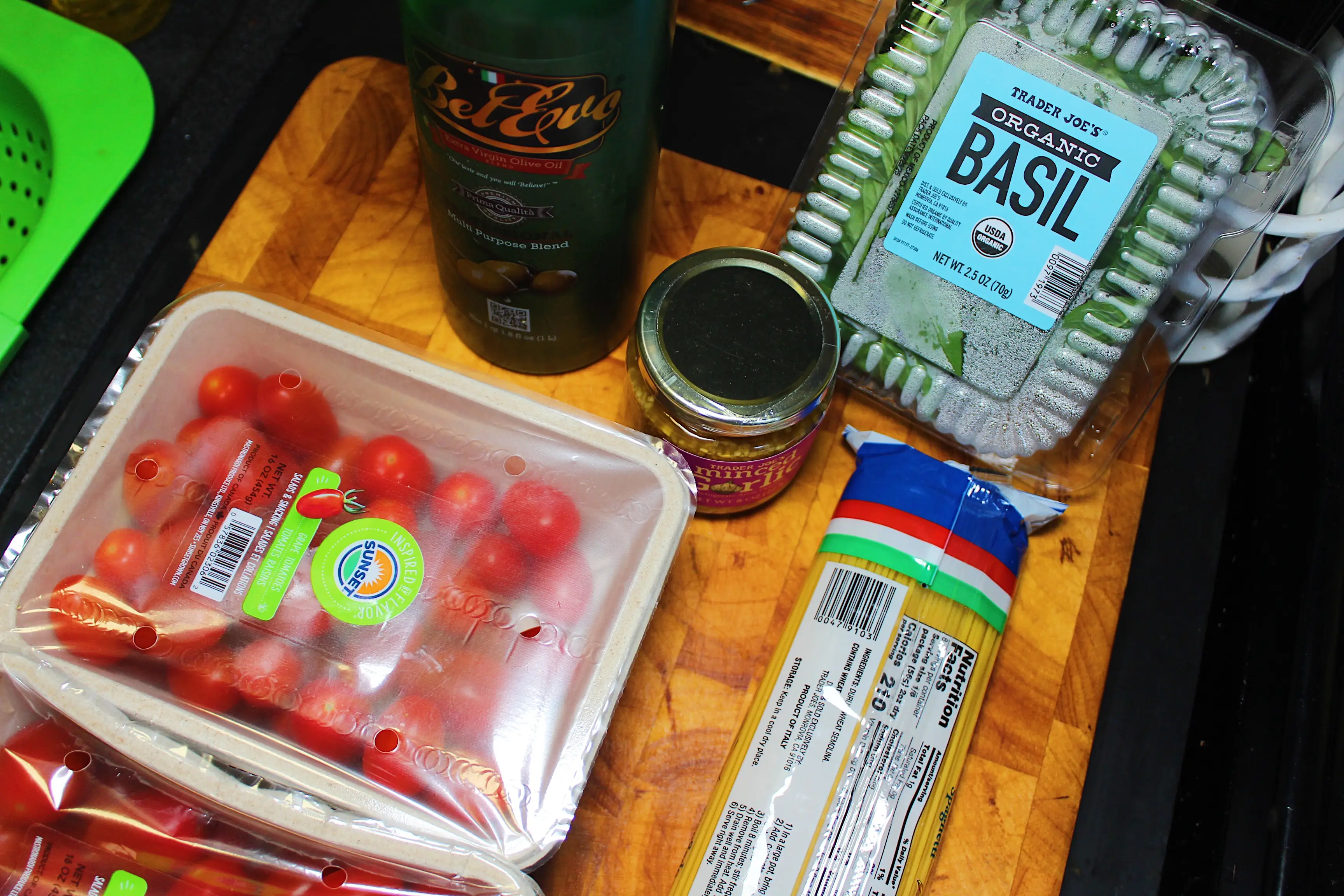 Tomatoes, minced garlic, spagehtti, olive oil, and basil on a chopping board.