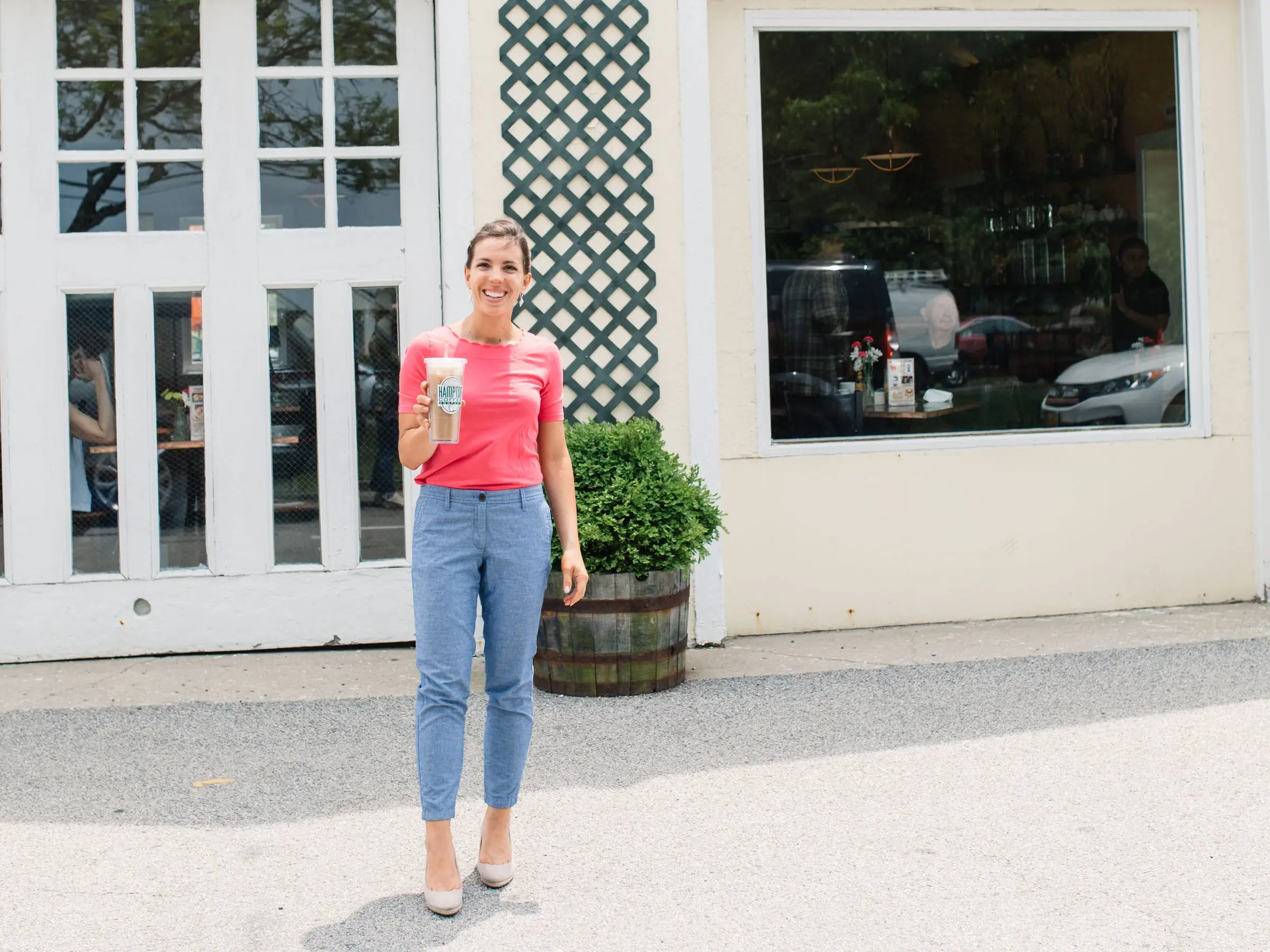 Vanessa holds a cup of coffee in front of the Hampton Coffee Company.