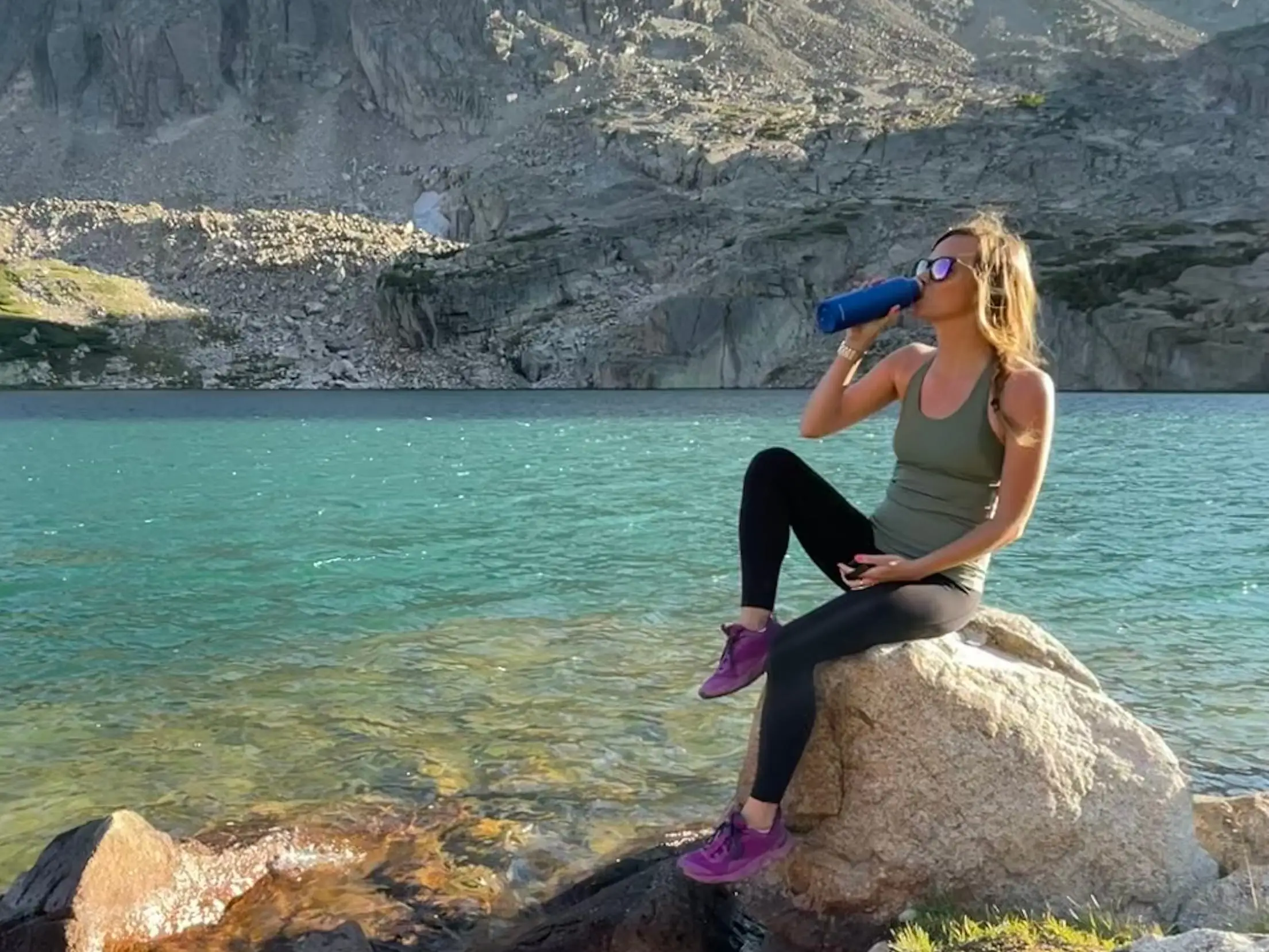 Emily sitting on a rock drinking out of a water bottle.