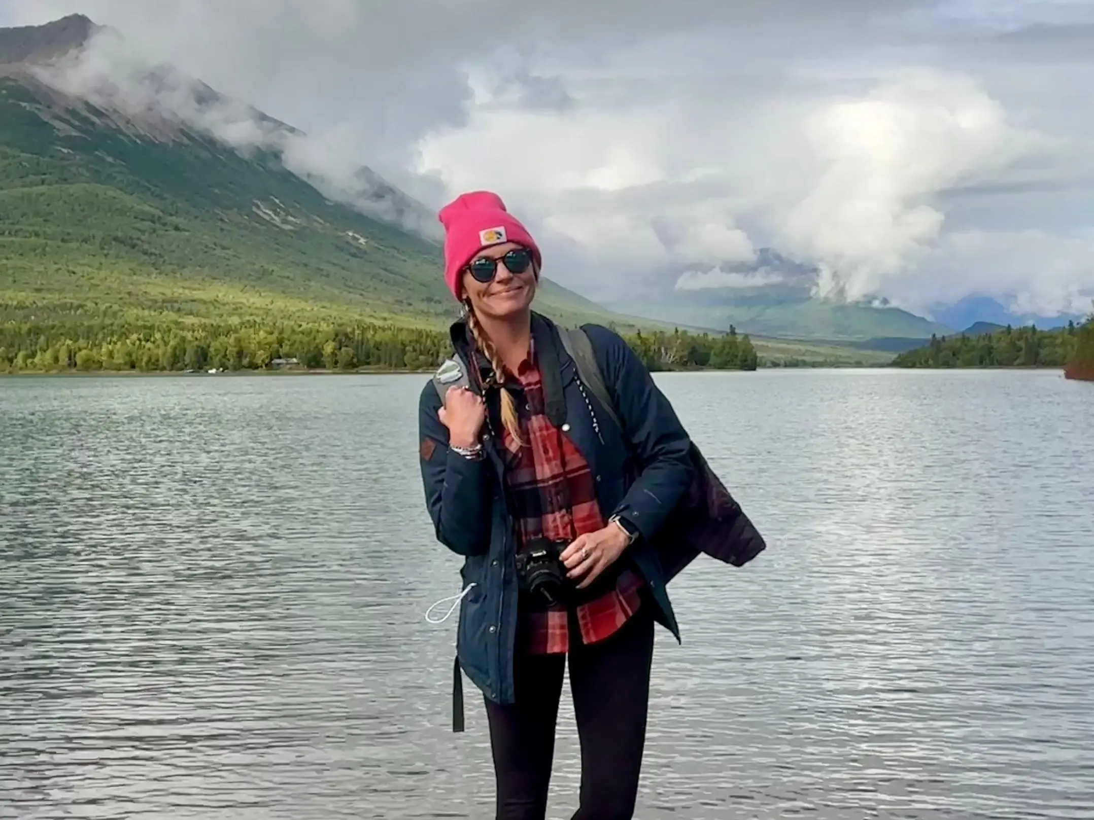 Emily standing in front of water wearing a flannel, coat, and hat.