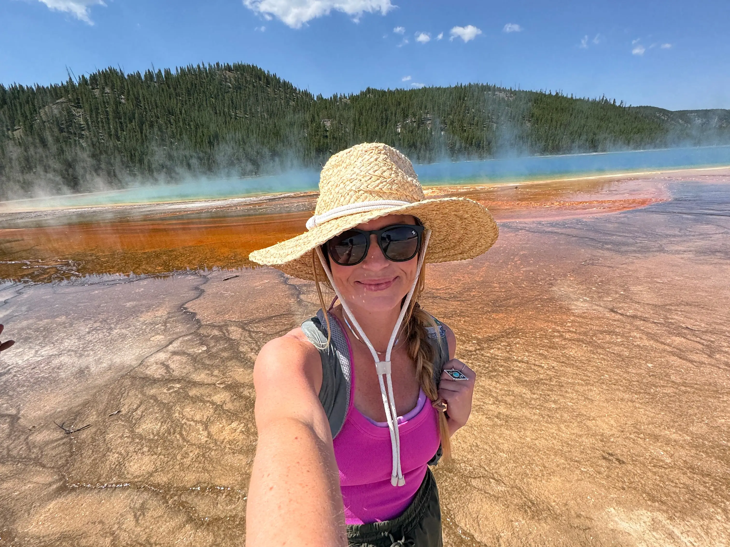 Emily taking a selfie in front of water wearing a wide brimmed hat.