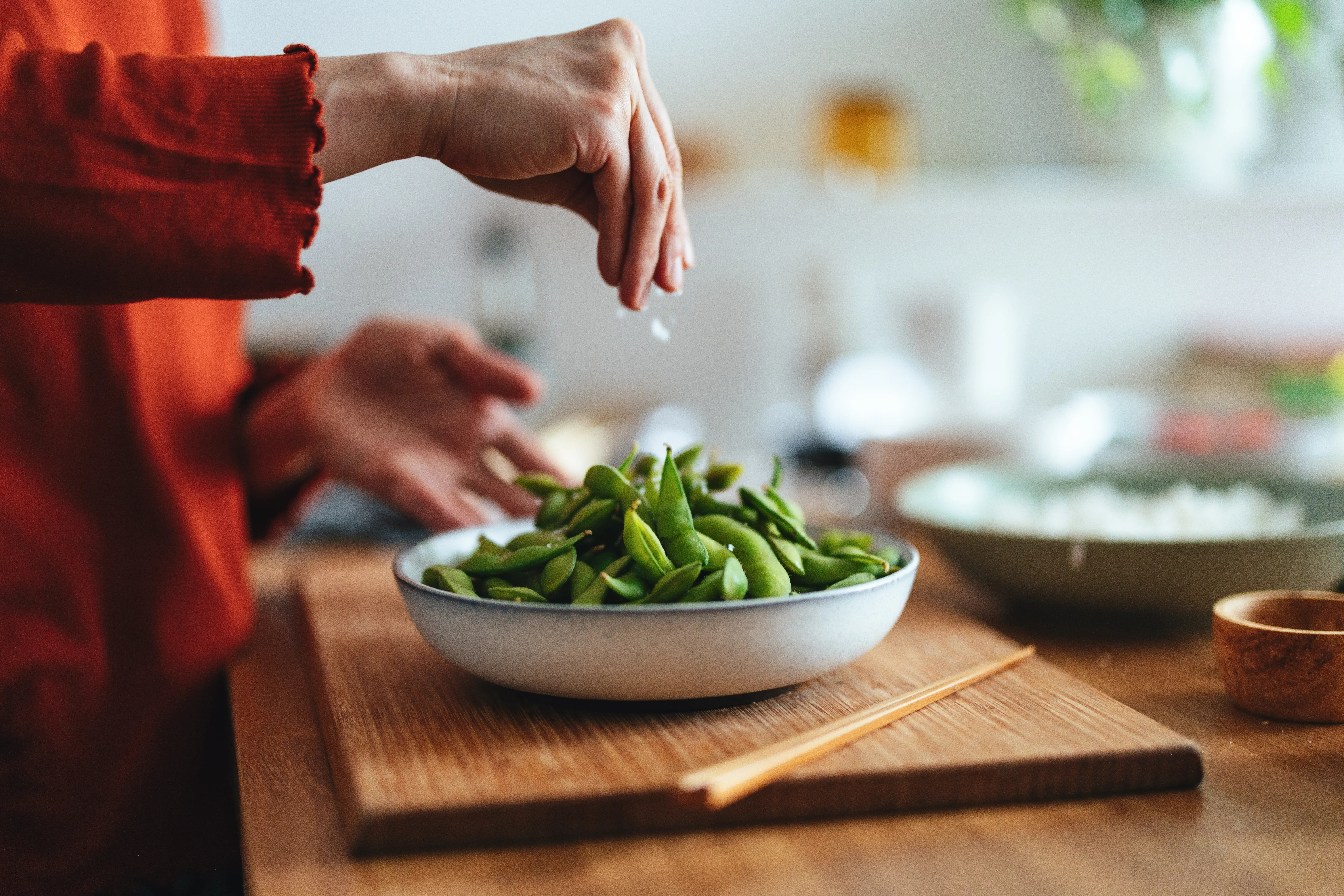 A person sprinkles salt over a bowl of edamame.