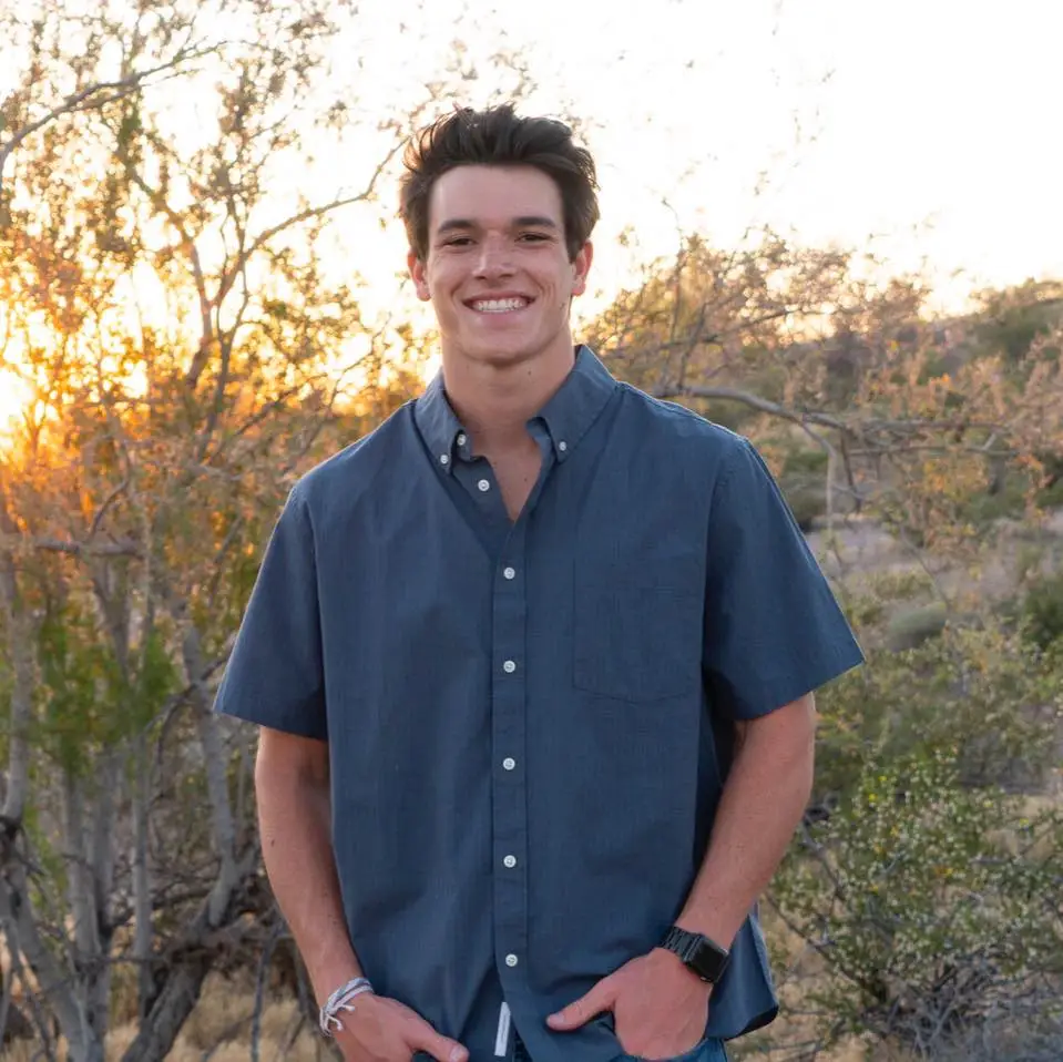 A young man standing in front of a tree takes a selfie.