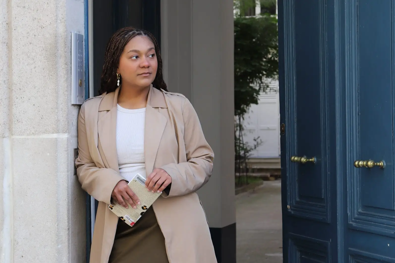 Author Naydeline Mejia leaning on doorway next to blue door, looking to the side