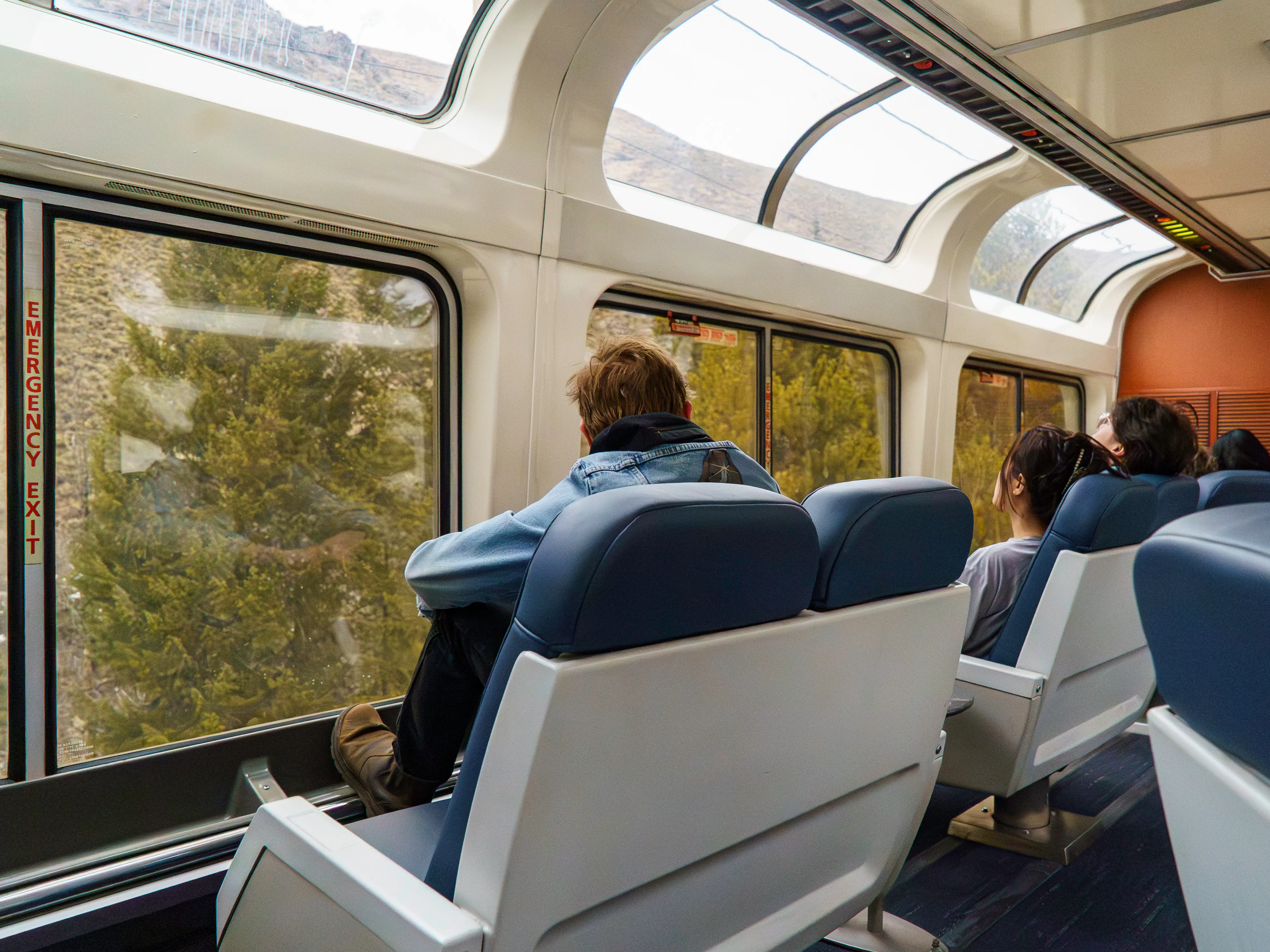 Passengers on an Amtrak train sit facing two rows of windows in the observation car