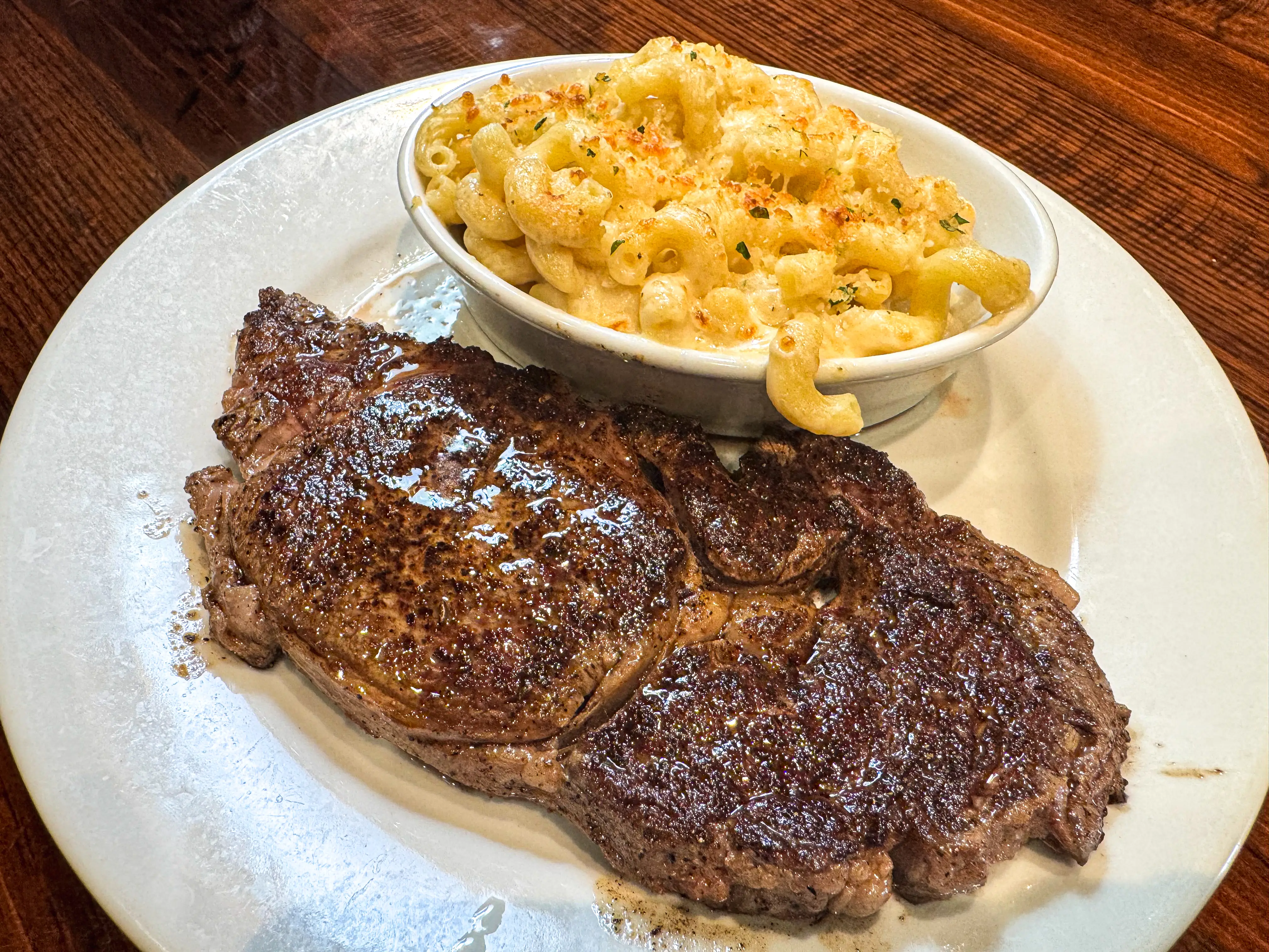 A piece of steak and a small bowl of mac and cheese on a white plate.