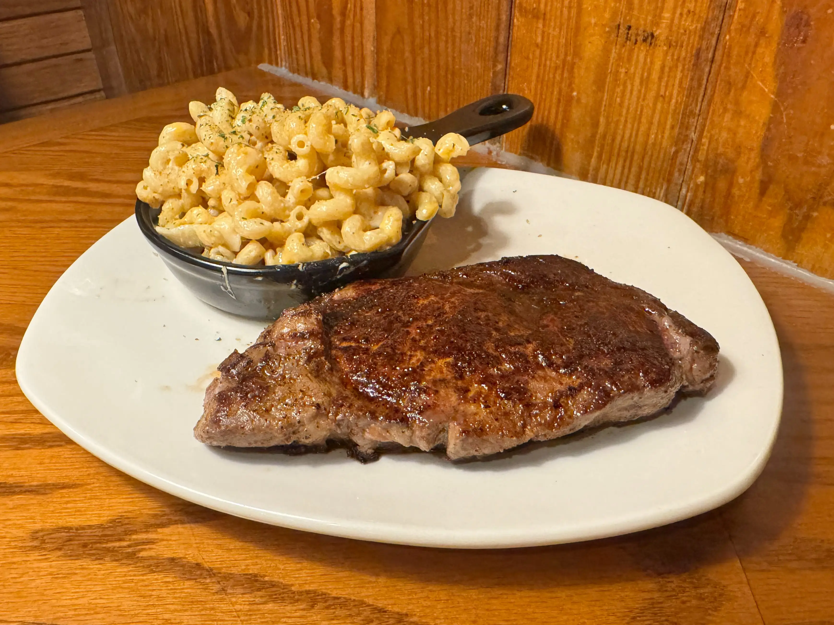 A steak and a small bowl of mac and cheese on a white plate.