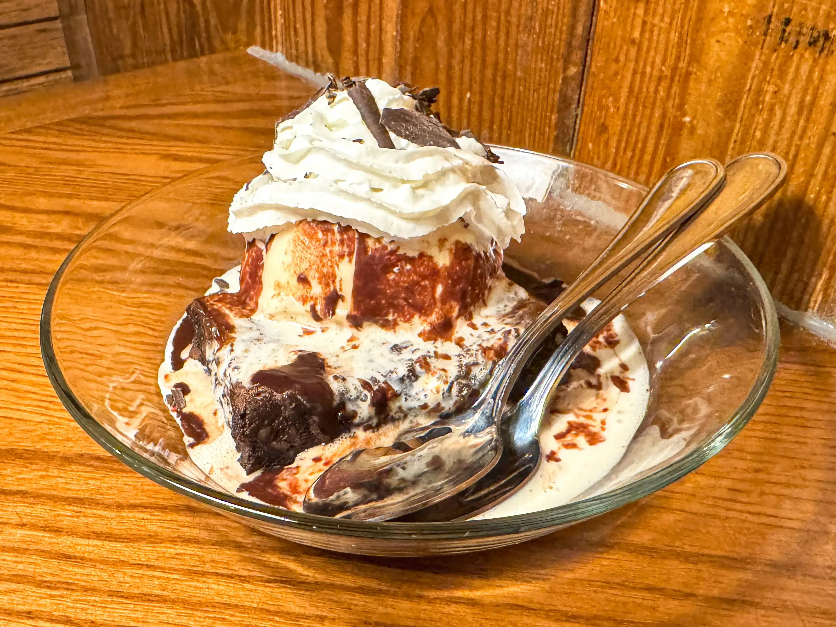 A brownie topped with vanilla ice cream and whipped cream in a clear bowl.
