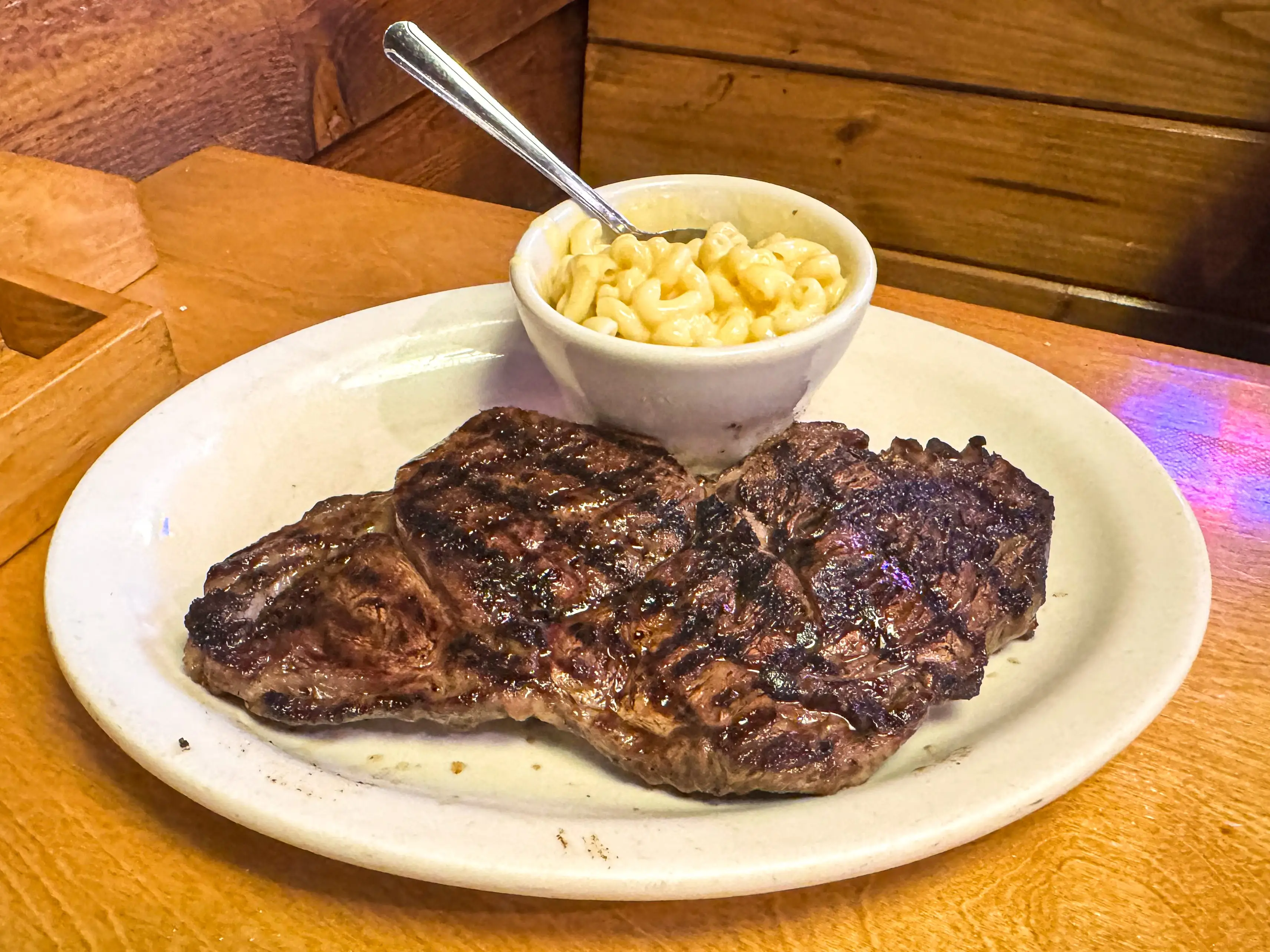 A steak and a small bowl of mac and cheese on a white plate.