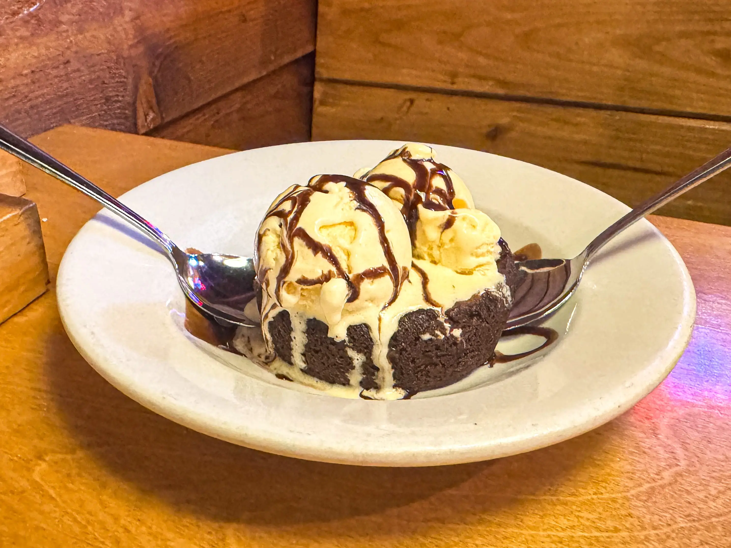 A brownie topped with vanilla ice cream in a white bowl.